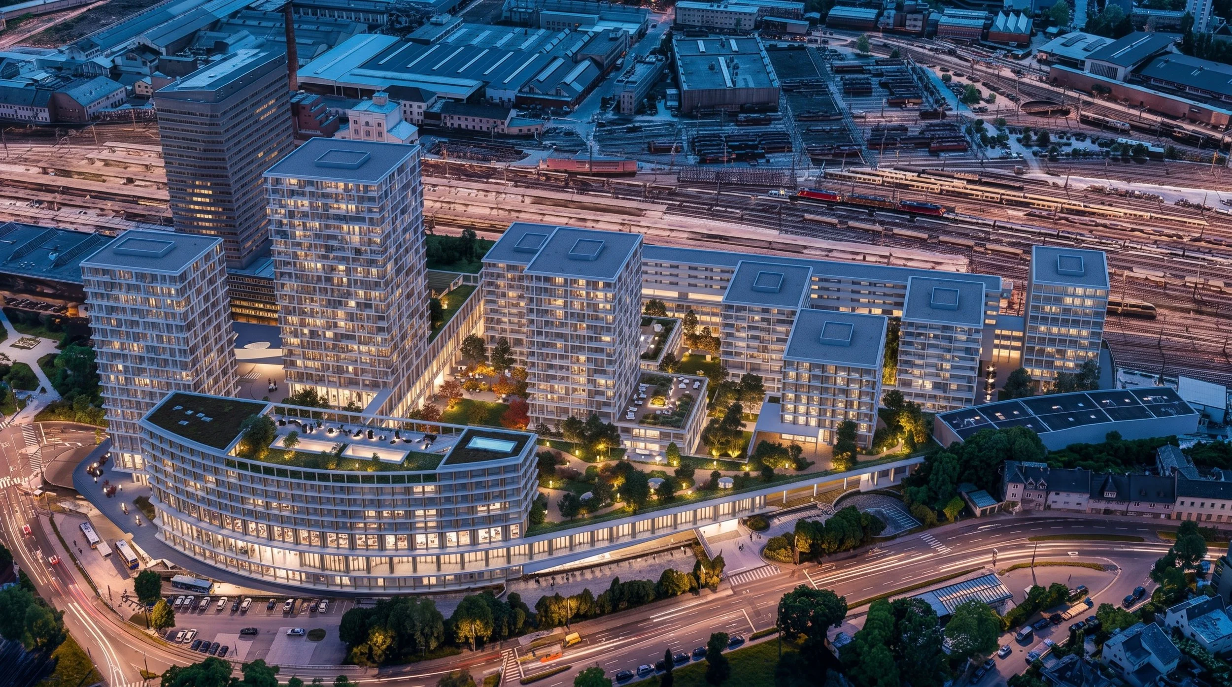 Aerial view of a cityscape during dusk, showcasing modern high-rise apartment buildings with balconies and green roofs, and a busy railway station with multiple train tracks and trains.