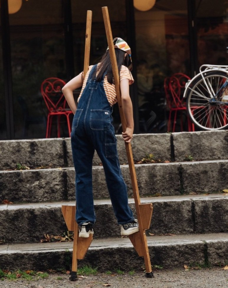 En jeansklädd tjej som går på styltor med ryggen mot kameran.