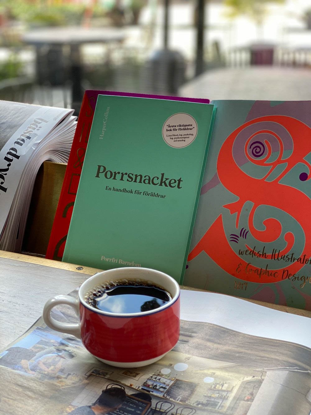 En turkos handbok för alla föräldrar med titel “Porrsnacket” ståendes i ett bokställ och en kaffekopp i förgrunden.