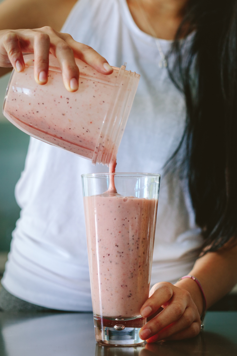 Person pouring a strawberry smoothie into a glass from a blender container.