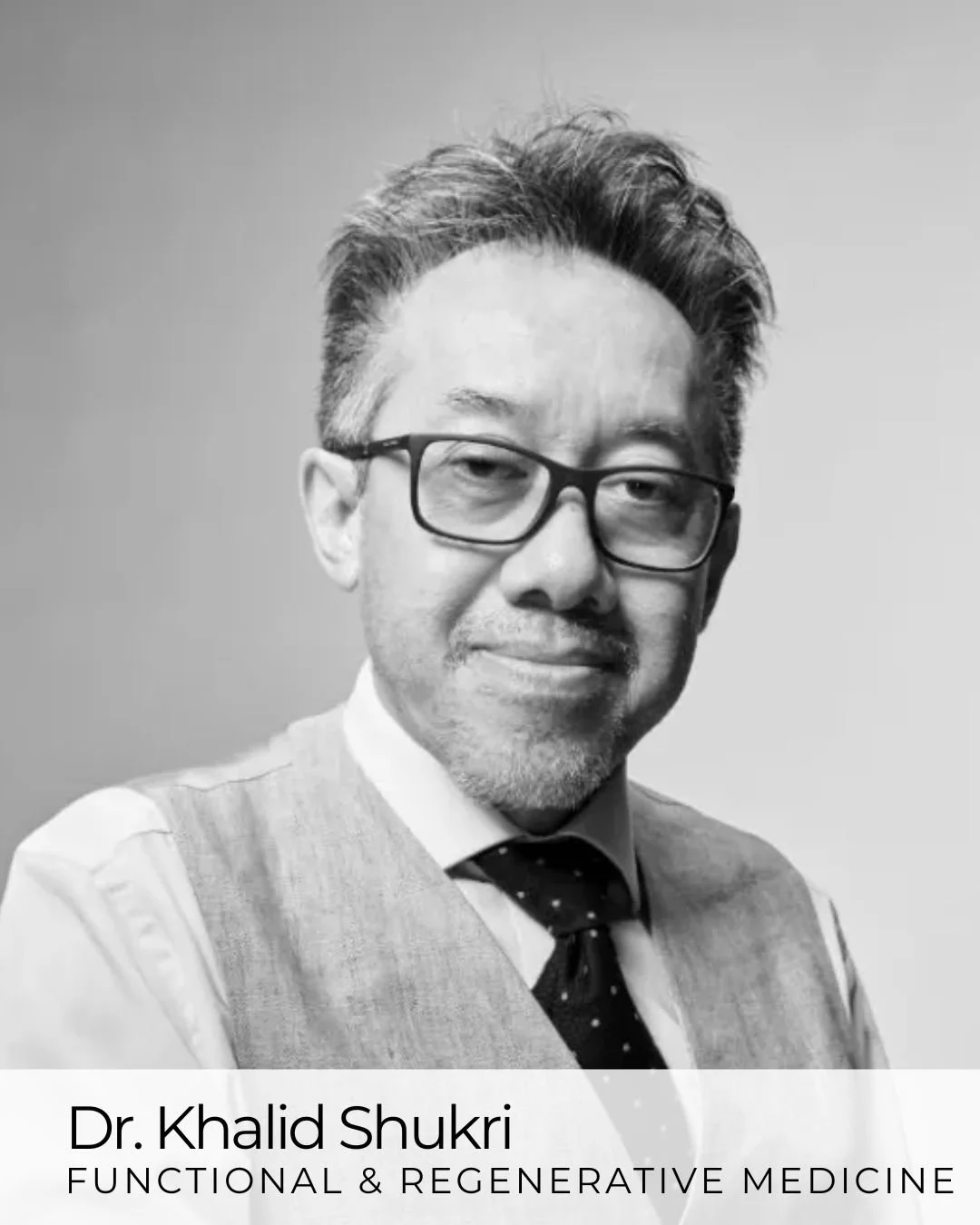 A black and white portrait photo of a man with glasses, styled hair, wearing a shirt, vest, and tie.