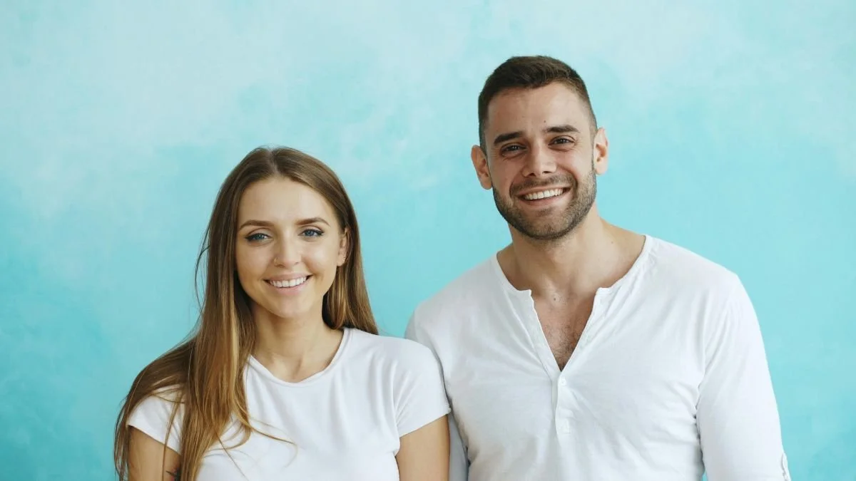 A smiling man and woman standing side by side against a light blue background.