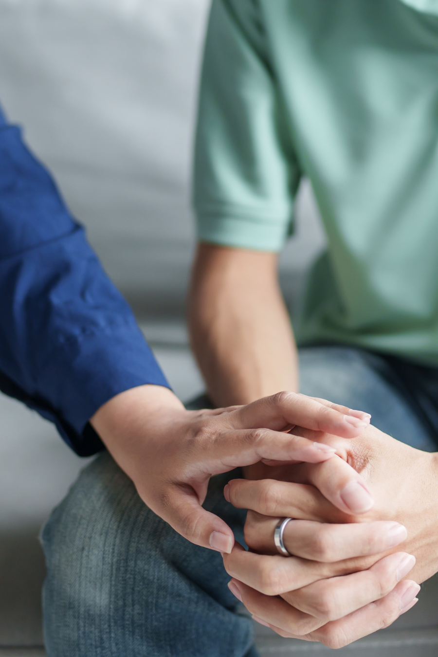 Two people holding hands, one person's hand resting on the other's knee, in a supportive gesture.