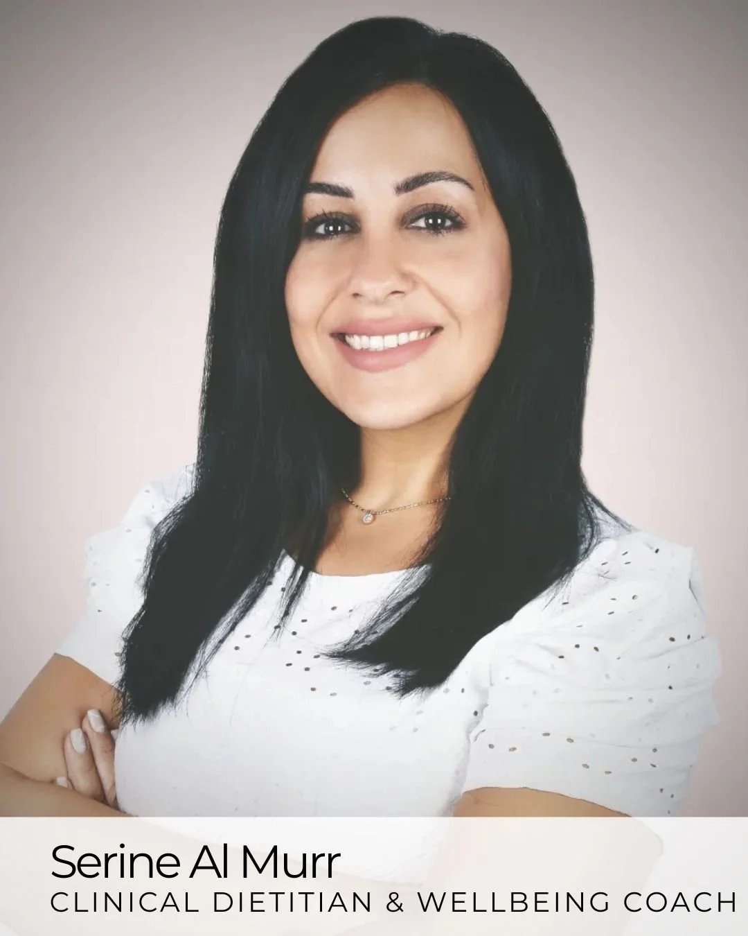 Portrait of a woman with long black hair, smiling, wearing a white shirt with small holes, and a delicate necklace, standing against a plain background.