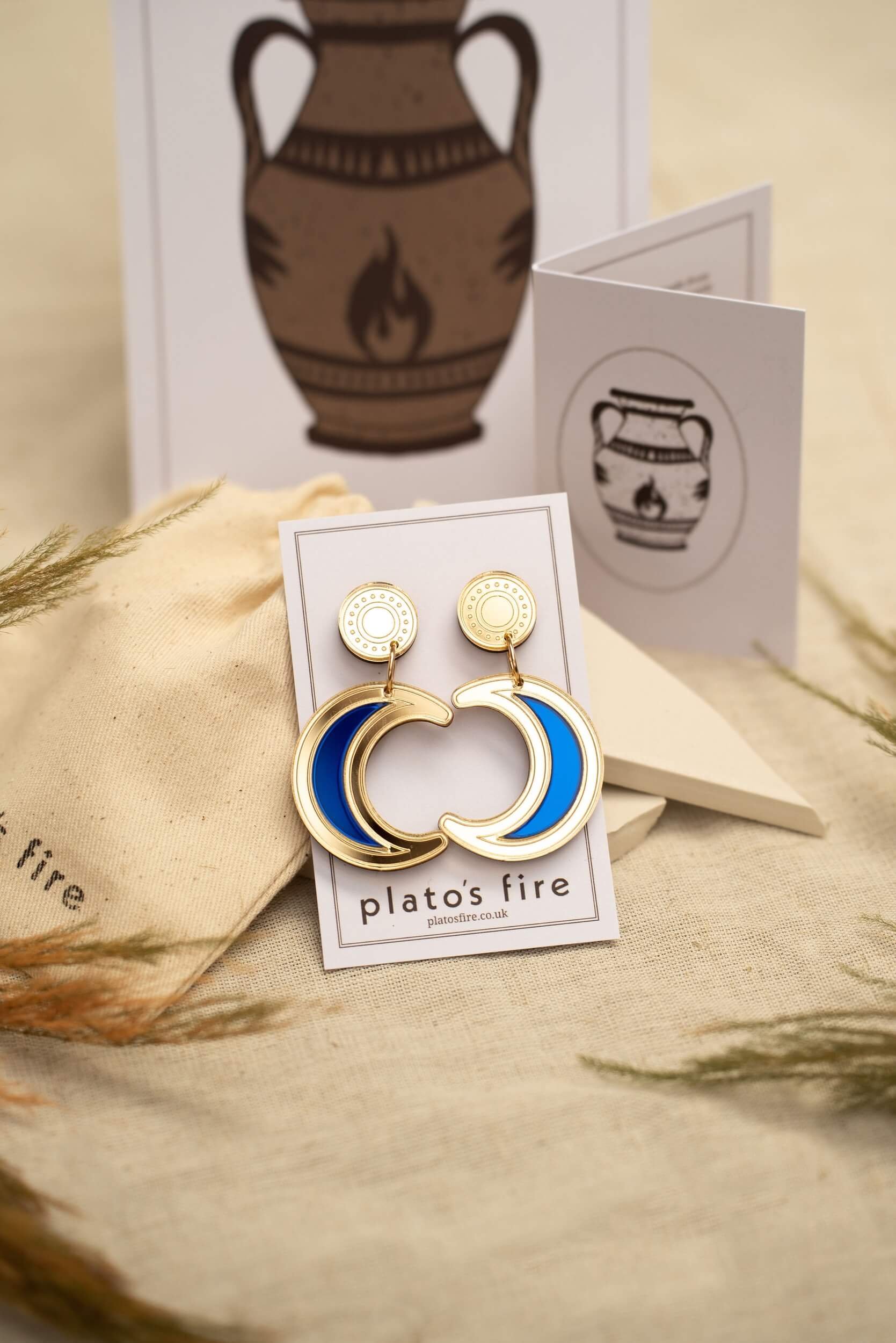 laser-cut acrylic crescent moon drop stud earrings in mirror gold and royal blue on a backing card