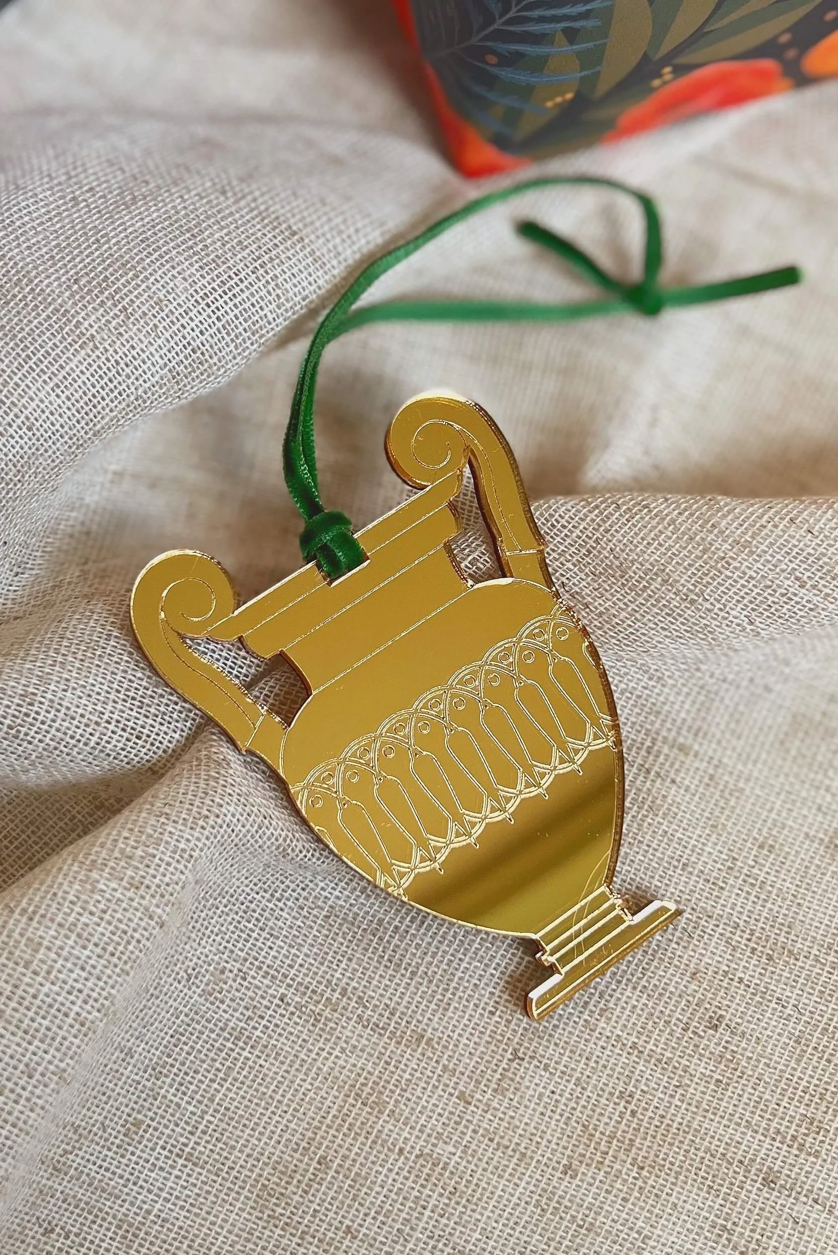 ancient greek krater christmas tree ornament in gold mirror acrylic laid flat on neutral coloured fabric