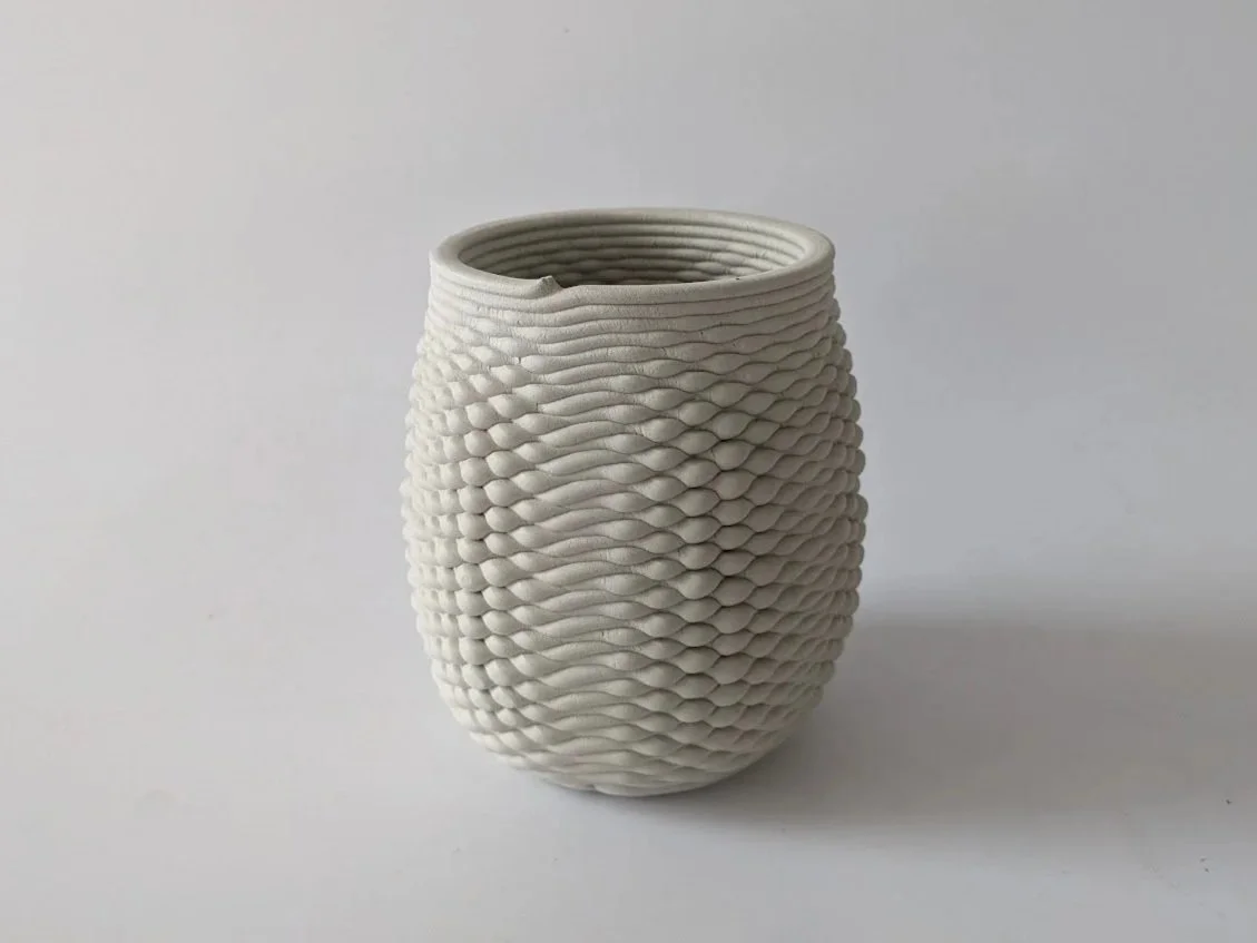 White 3D Printed ceramic vase with a textured, wavy surface design on a light gray background.