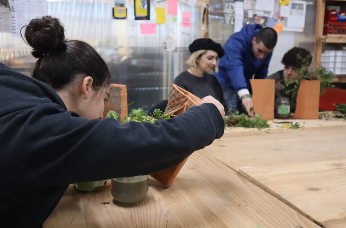 Four people working on a 3d printed gardening project at a workshop table, arranging plants and pots.