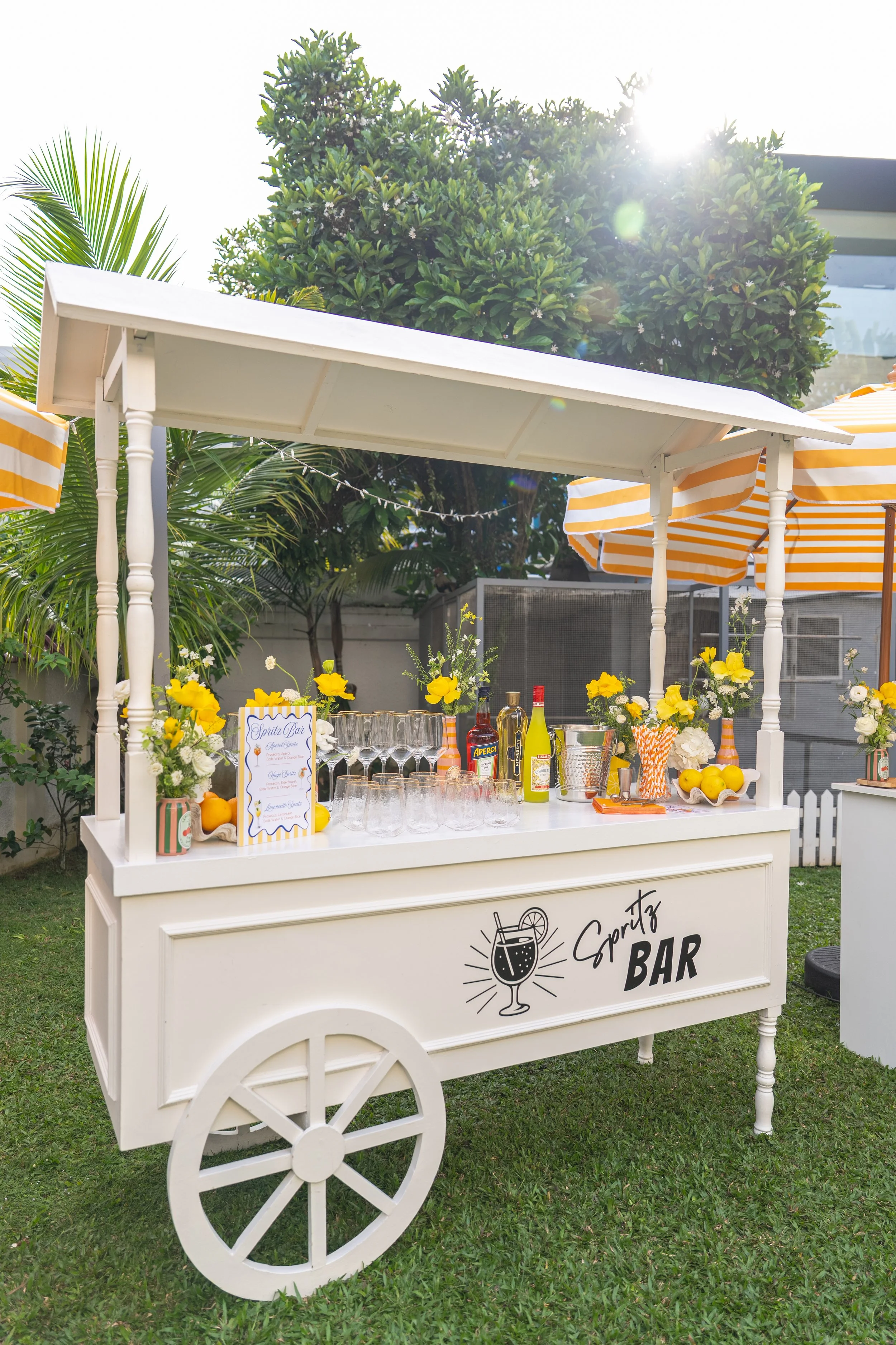 Stylishly curated Spritz Bar setup for events, featuring a bespoke cocktail cart serving Aperol, Hugo, and Limoncello Spritz. Perfect for garden parties, birthdays, corporate gatherings, and outdoor celebrations. Designed with vibrant florals, citrus