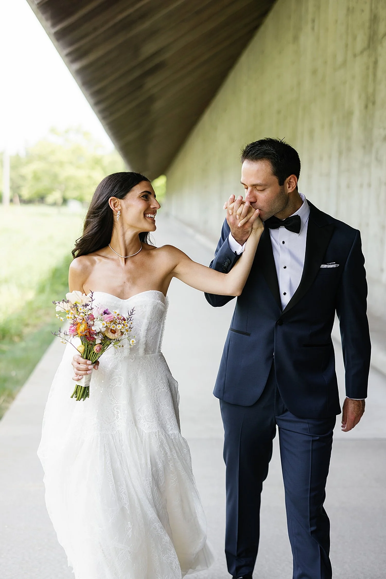  groom kisses bride’s hand as they walk together  