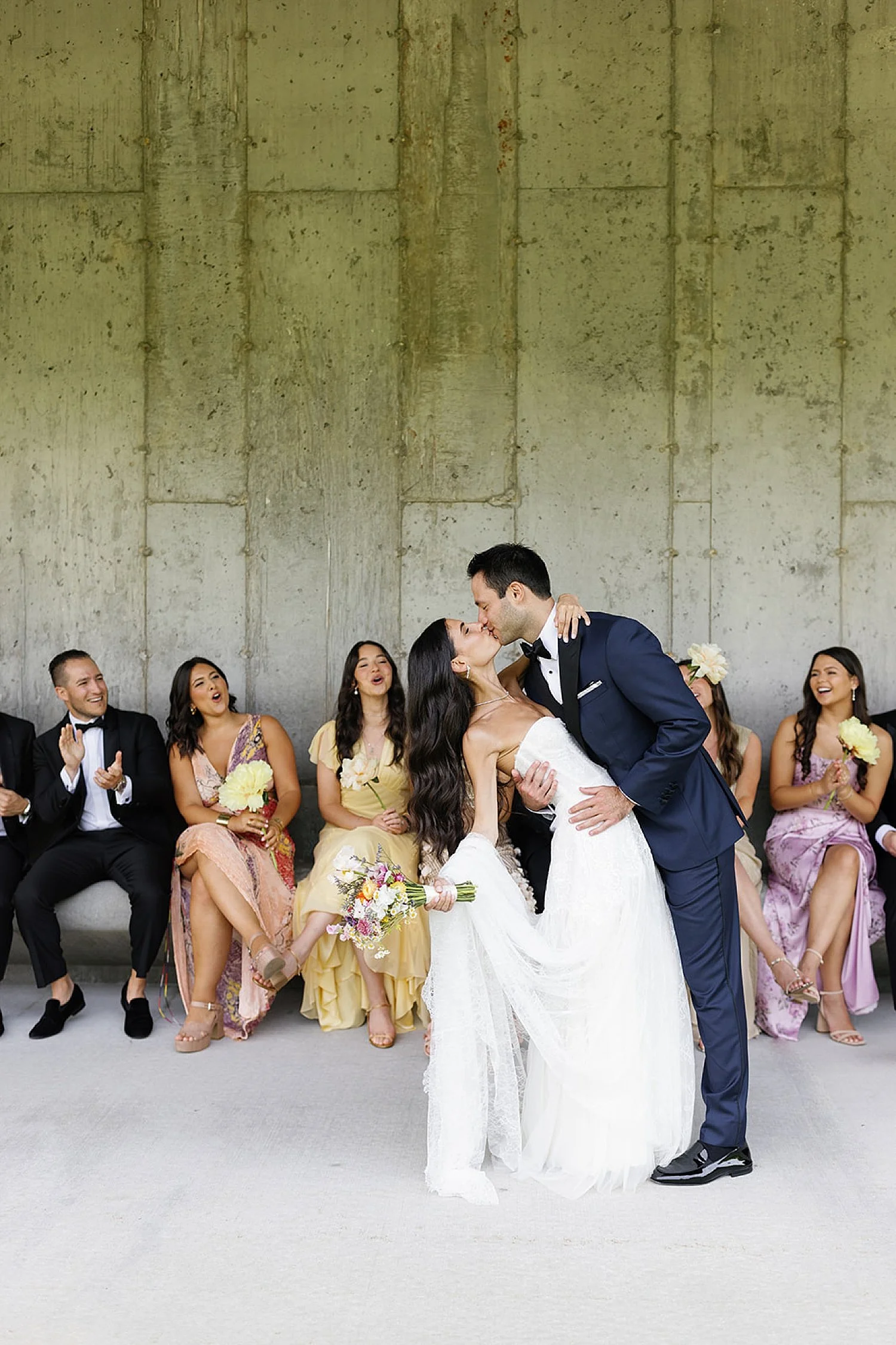  bride and groom kiss with wedding party around them 