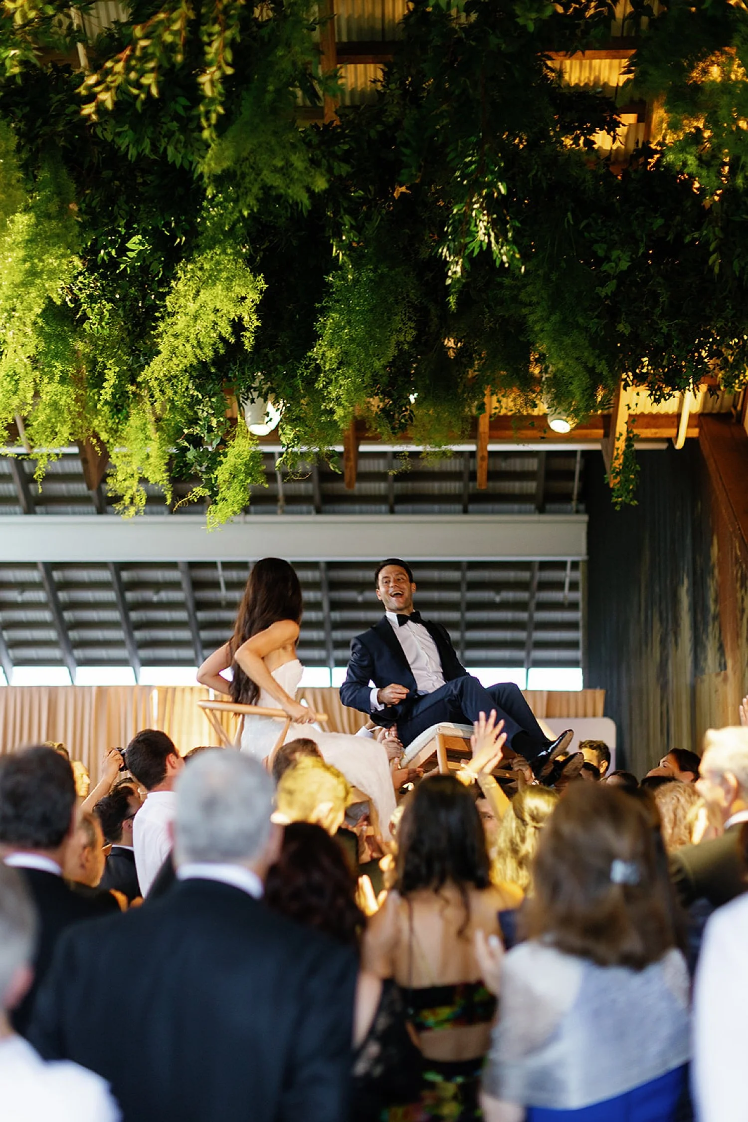  guests lift bride and groom up in the air on chairs 
