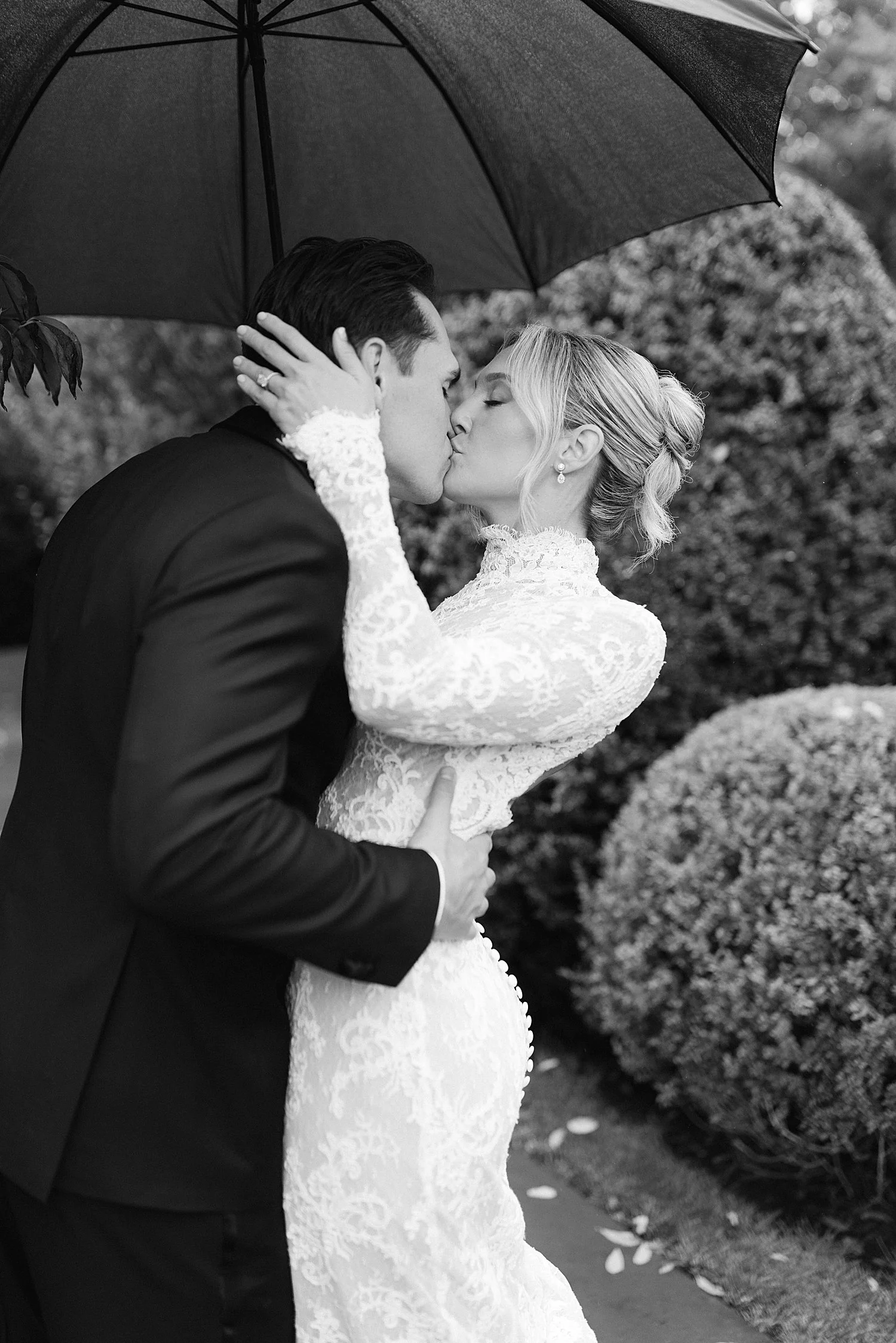  bride and groom kiss in the rain underneath an umbrella 