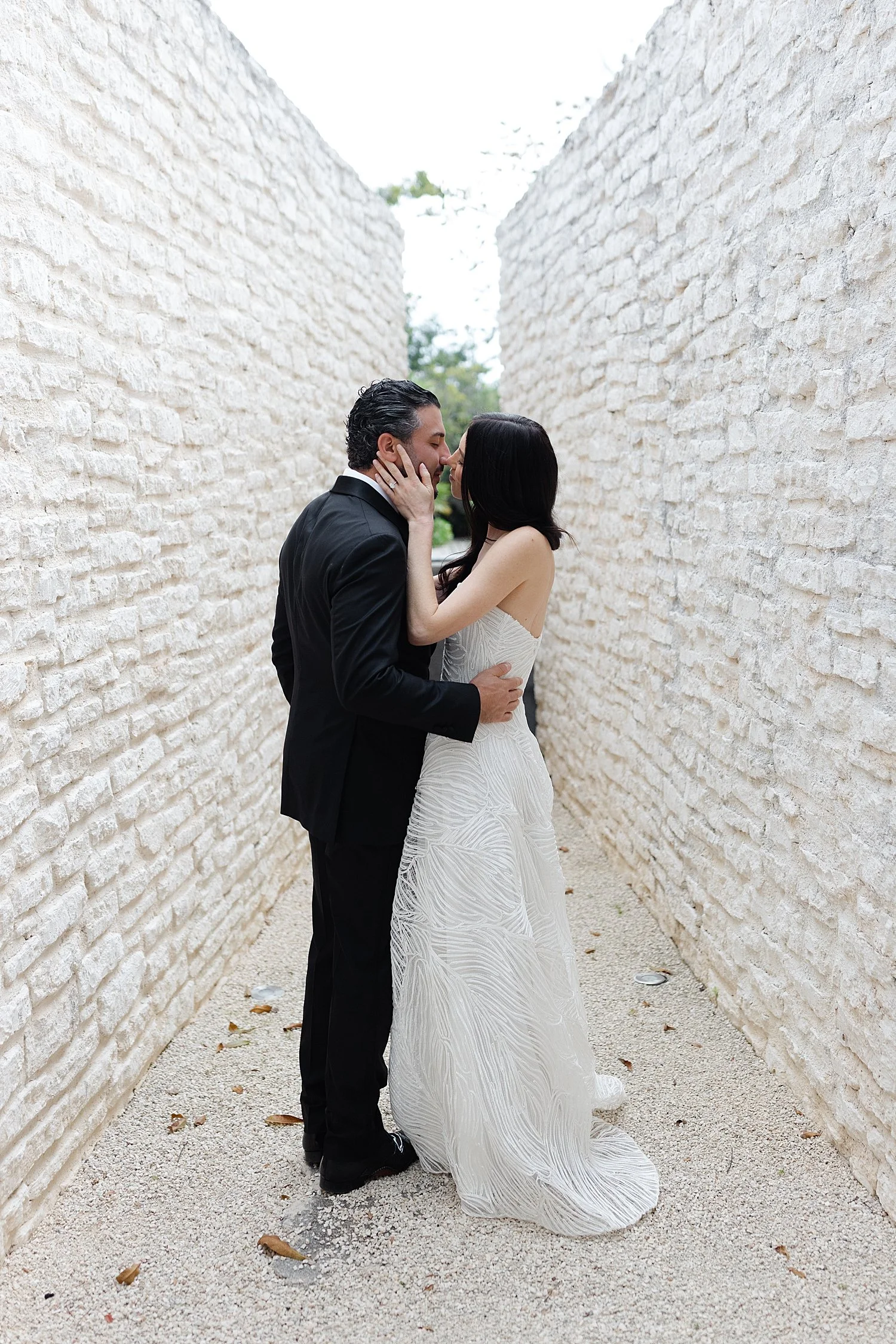  bride and groom kiss in between two white brick buildings 