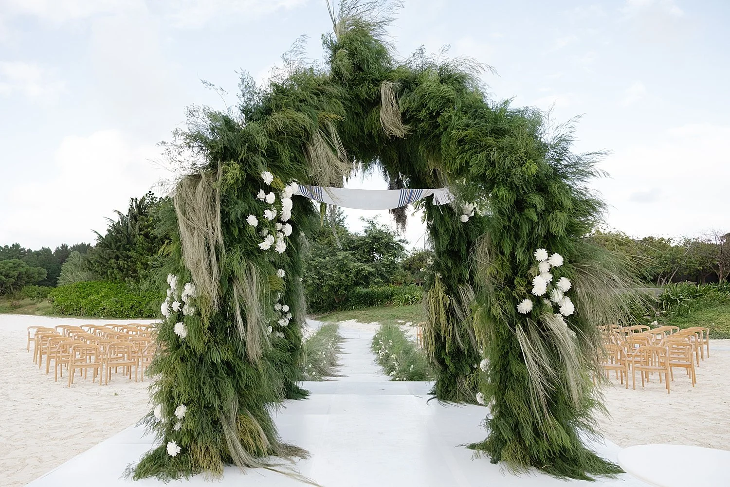  chuppah decorated with long grasses and flowers blowing in the wind on beach  