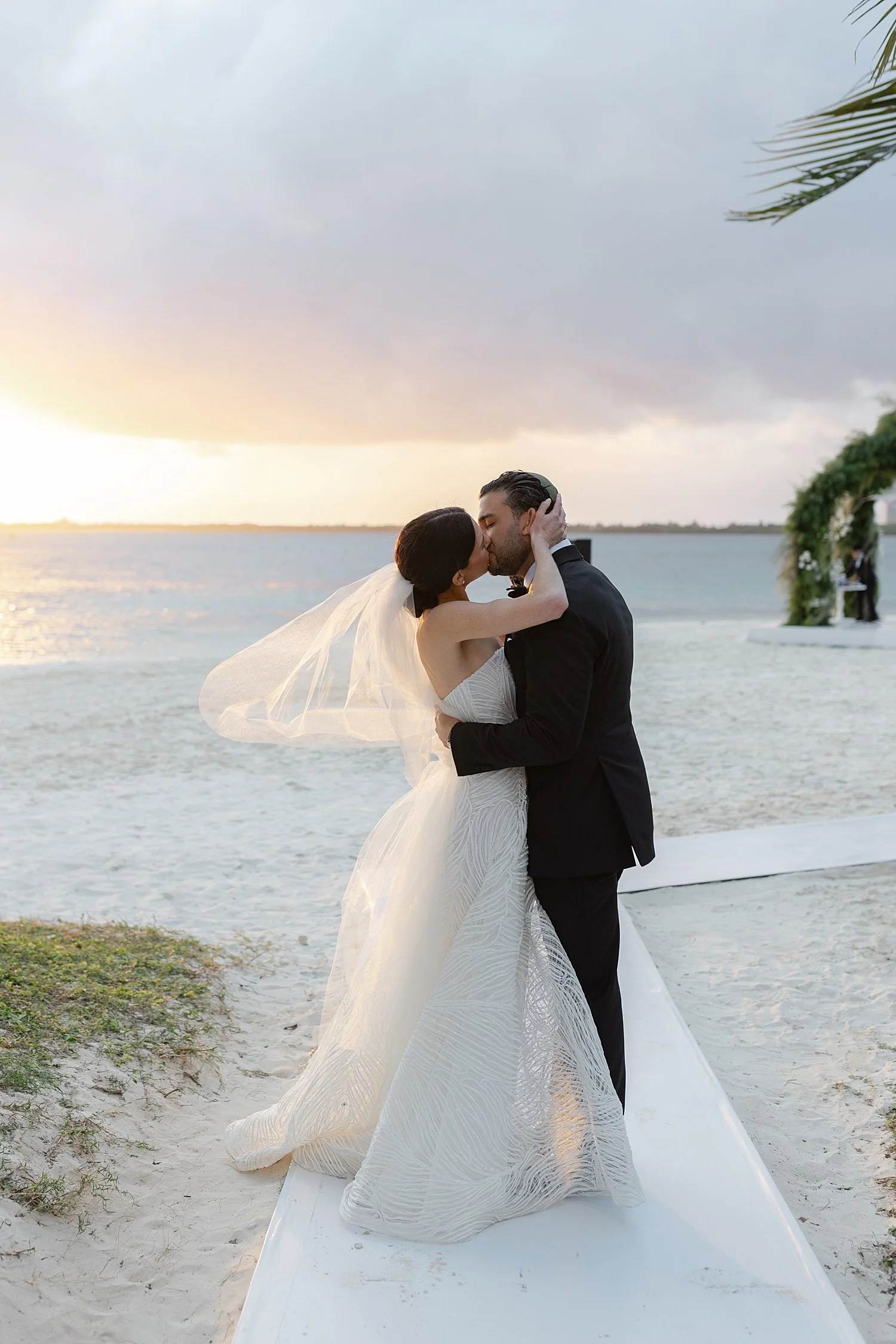  newlyweds kiss by the water with sun setting at Mexico resort 
