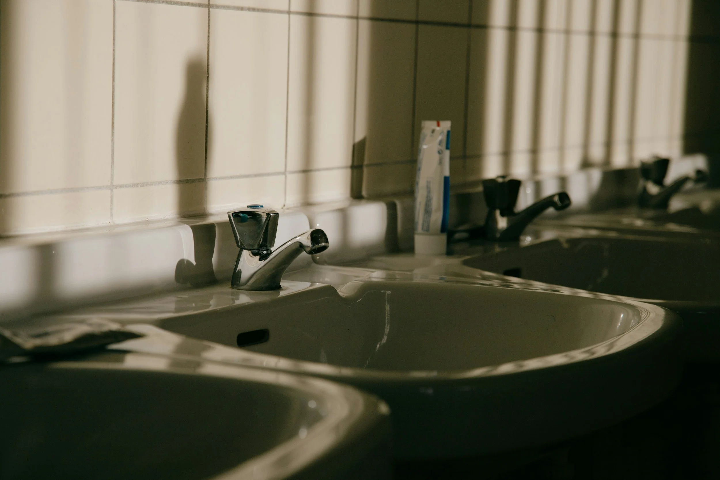 A tube of toothpaste sits on top of a row of bathroom sinks