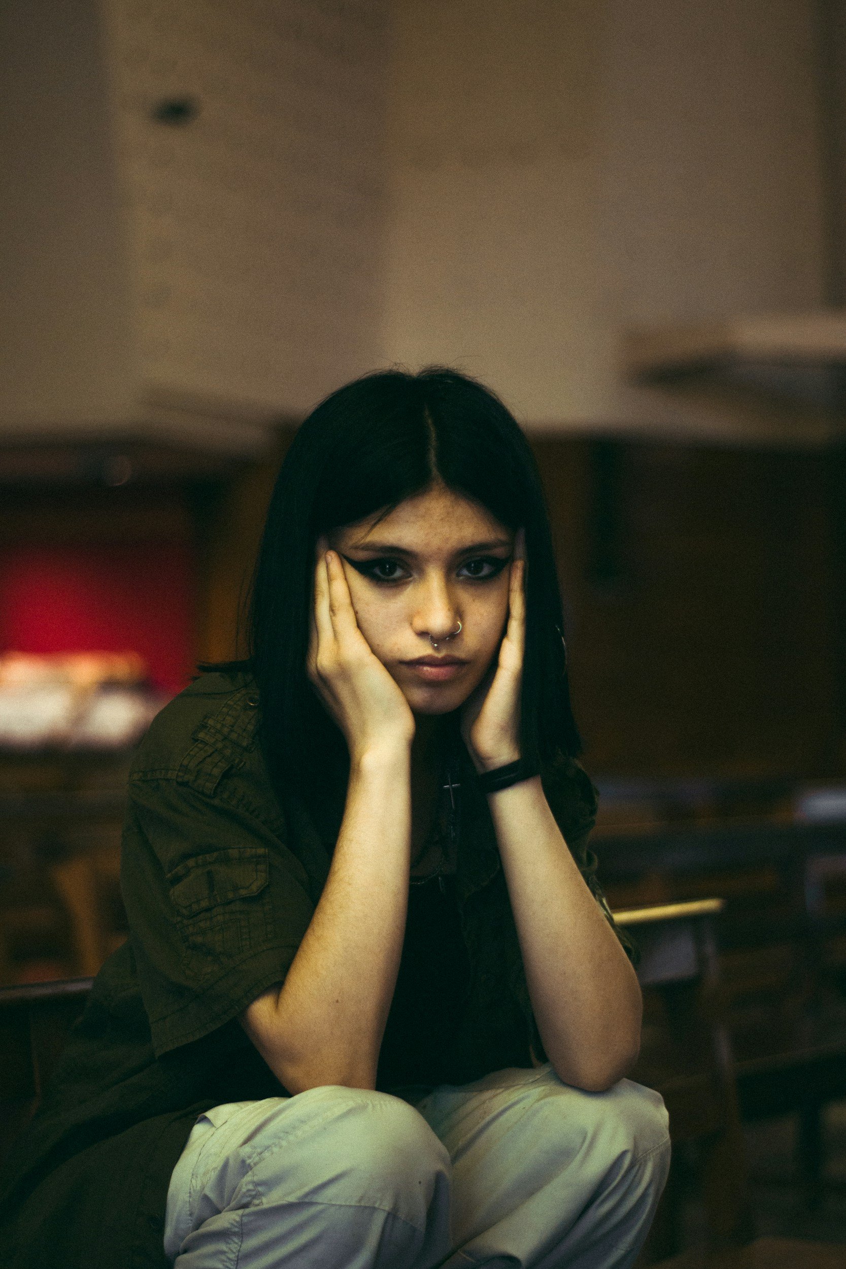 Teen girl representing a neurodivergent, ADHD, or autistic adolescent, sits with her chin in her hands, looking defensive and distressed