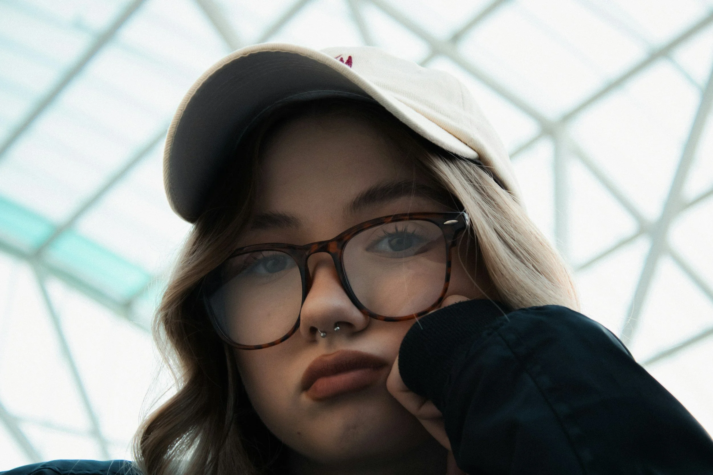 Teen girl wearing glasses and a baseball cap sitting with her head in her hand looking overwhelmed.