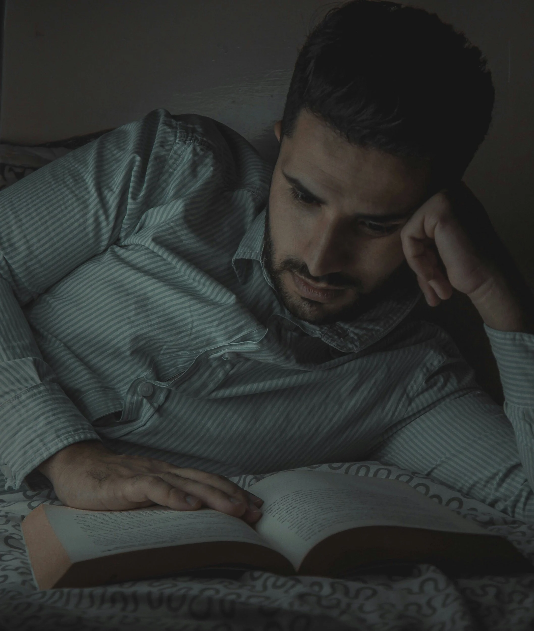 A tired man lies in bed reading at night with a concerned expression, reflecting the mental load and constant problem-solving often experienced by burned out dads.