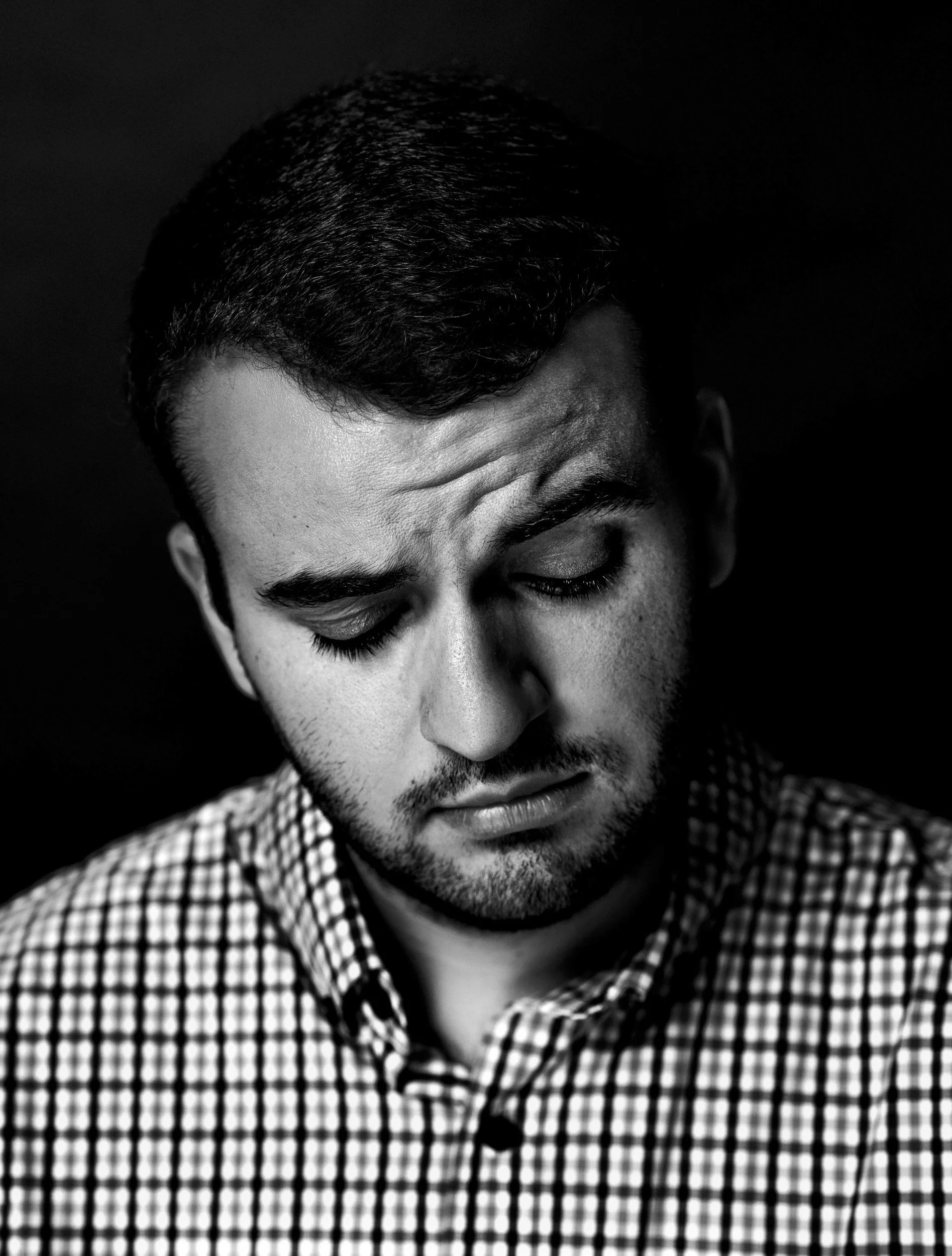 A black and white portrait of a man looking down with a serious, tired expression, representing emotional strain, frustration, and exhaustion associated with parental burnout.