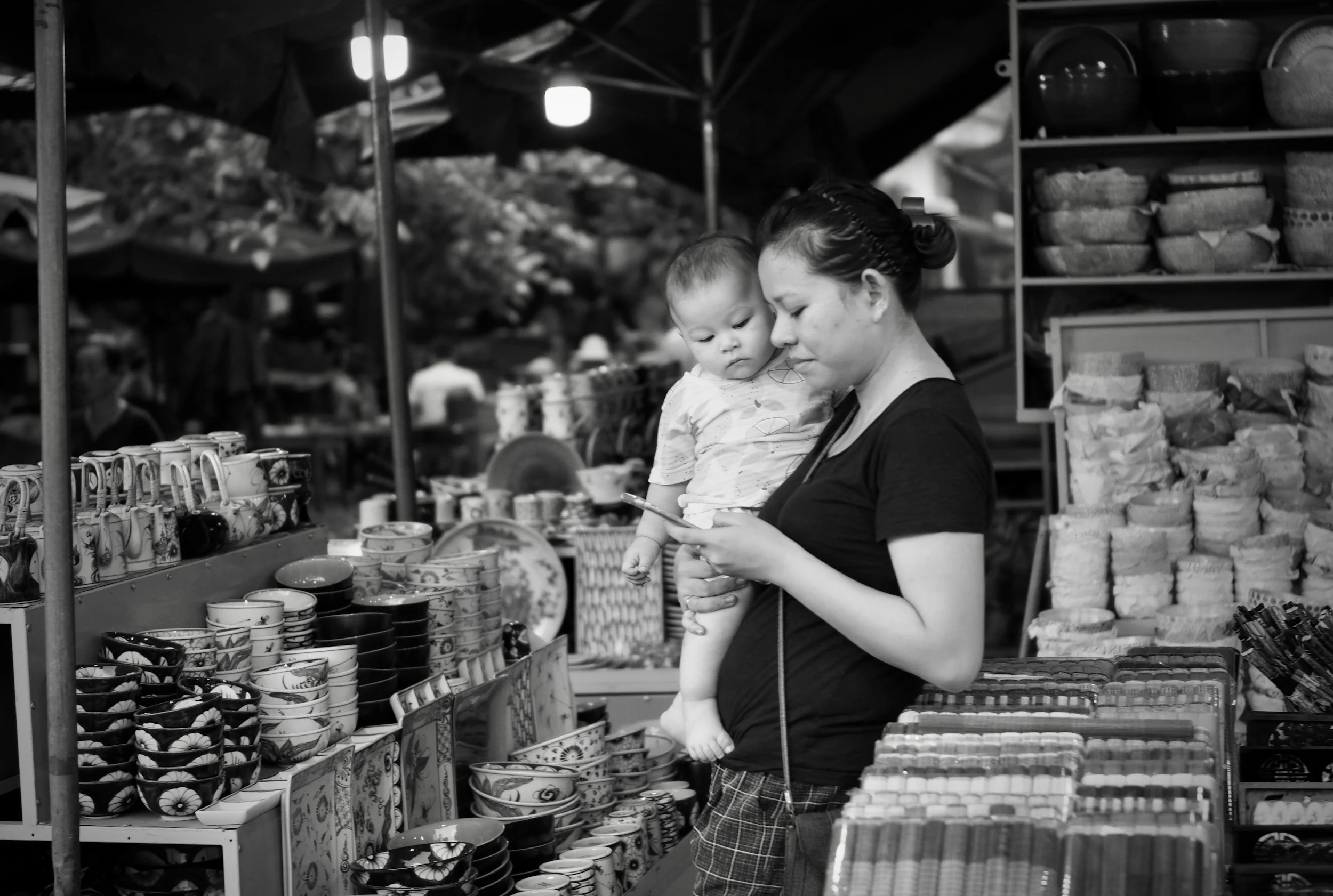 Mother holding her young child while shopping at an outdoor market.