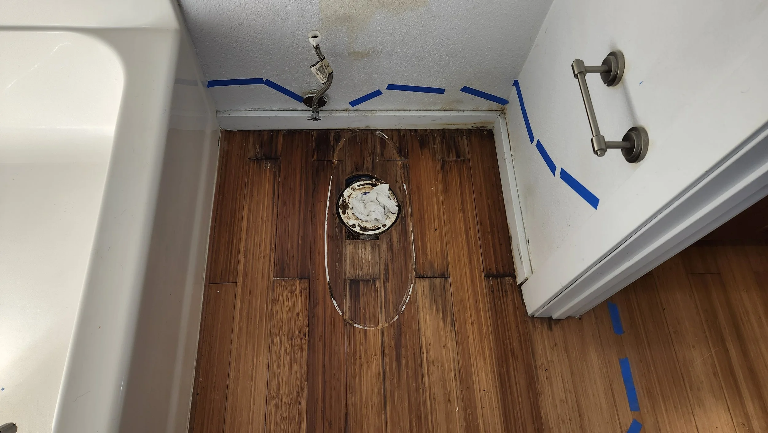Bathroom with exposed toilet drain, missing toilet, with blue painter's tape on walls and floor, and a small sink on the left side.