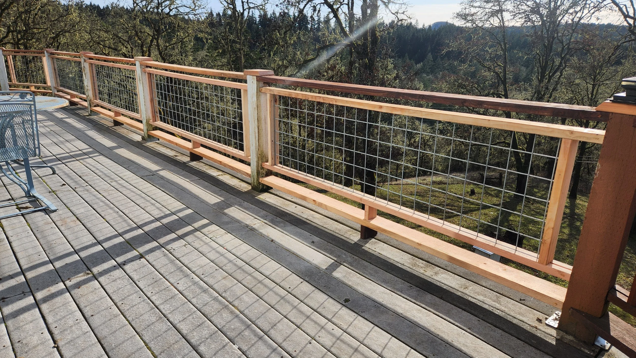 A wooden deck with a newly built safety railing overlooking a wooded landscape.