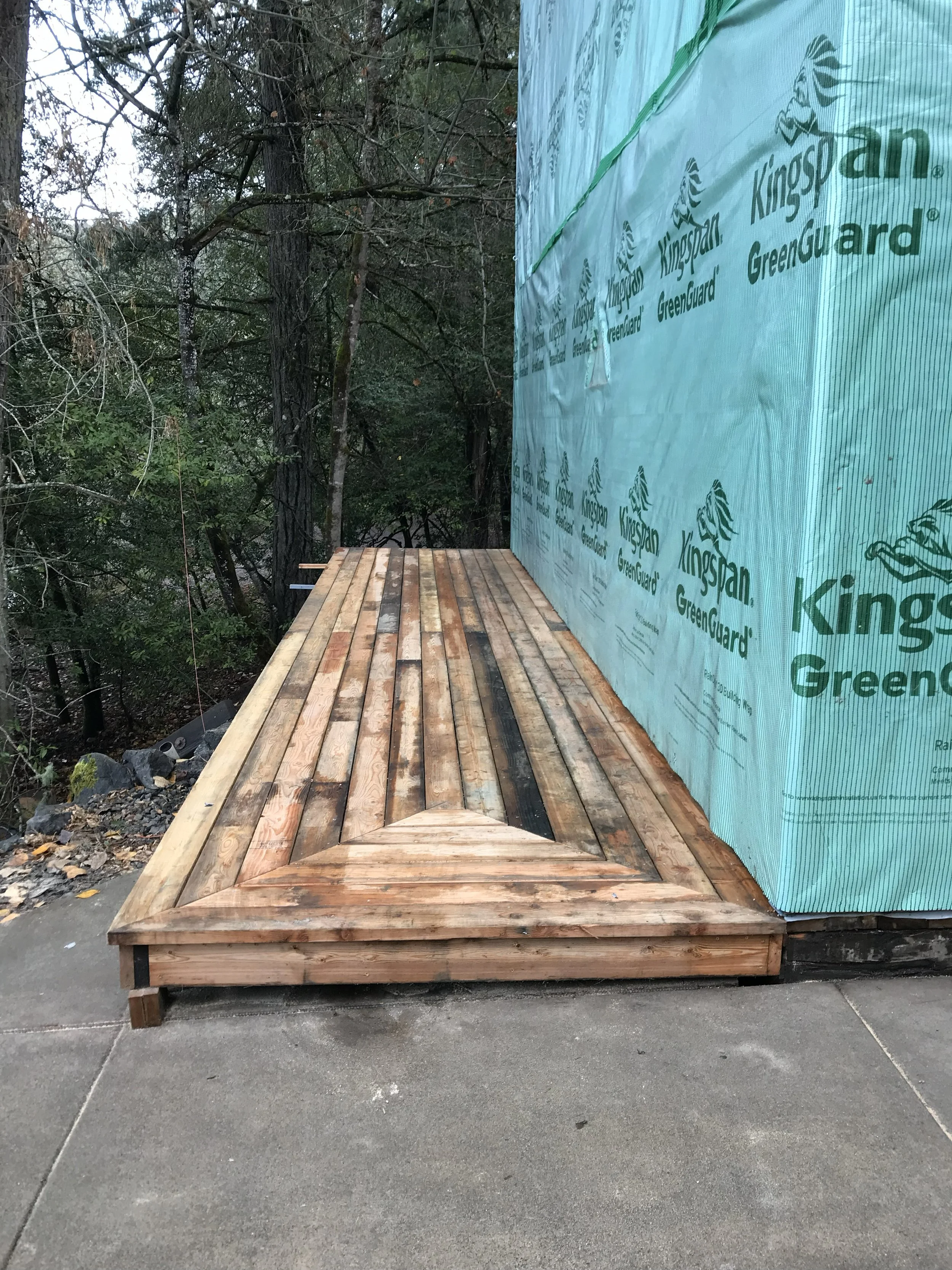Wooden deck under construction next to a building wrapped in blue GreenGuard siding, with trees nearby near Winchester Oregon