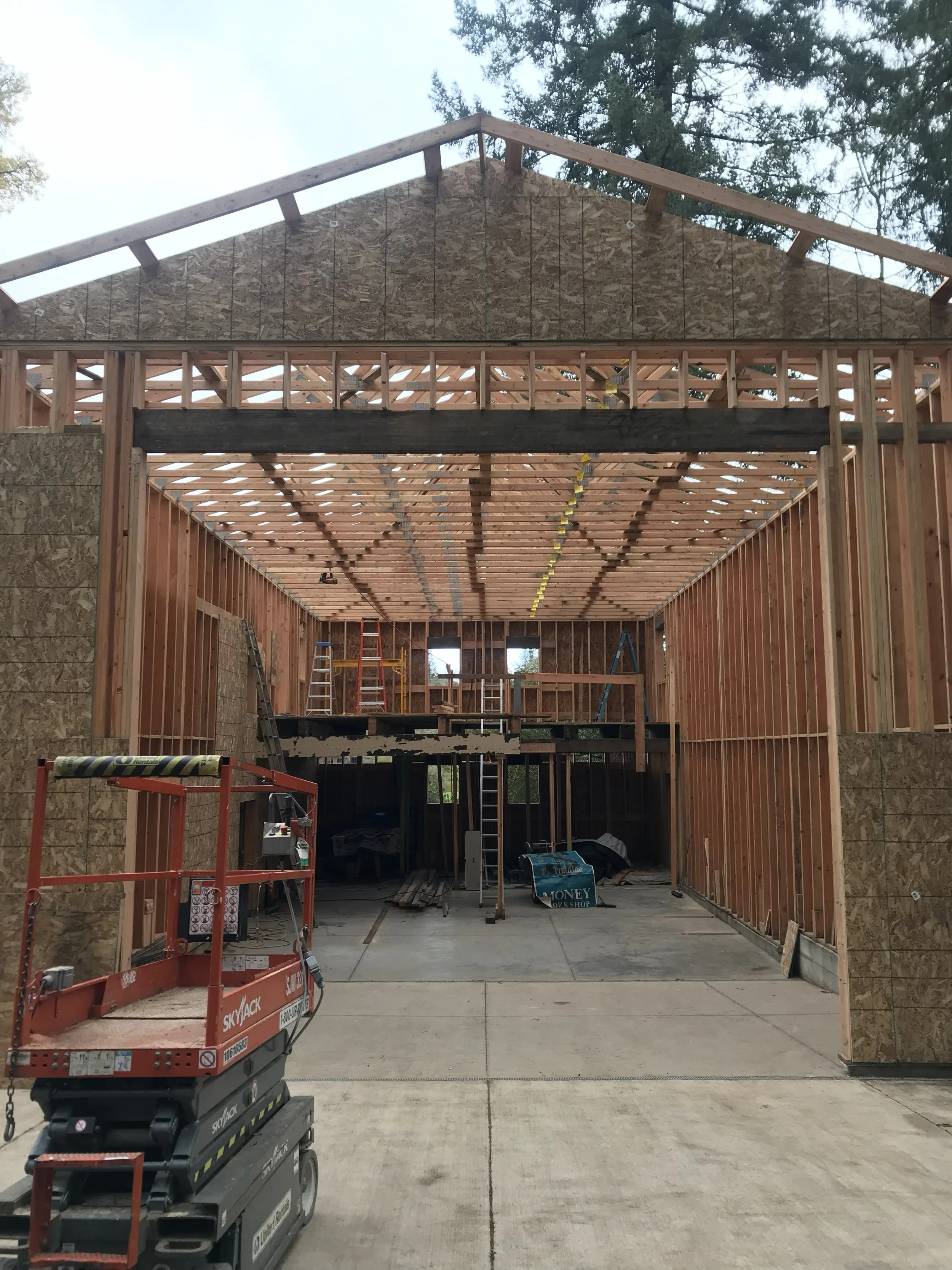 Construction site of a house with wooden framing, scaffolding, and ladders inside, and construction equipment in the foreground residential general contractors building a garage attached to existing home near Winchester Oregon.