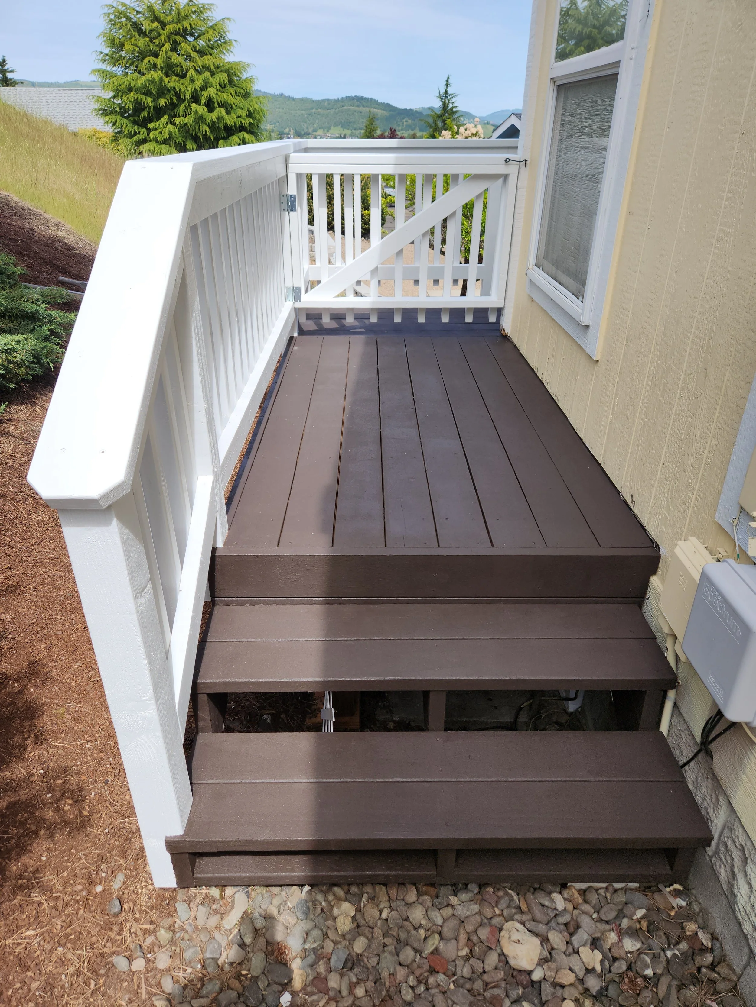 Rebuilt small outdoor deck with brown wooden steps and white railing.