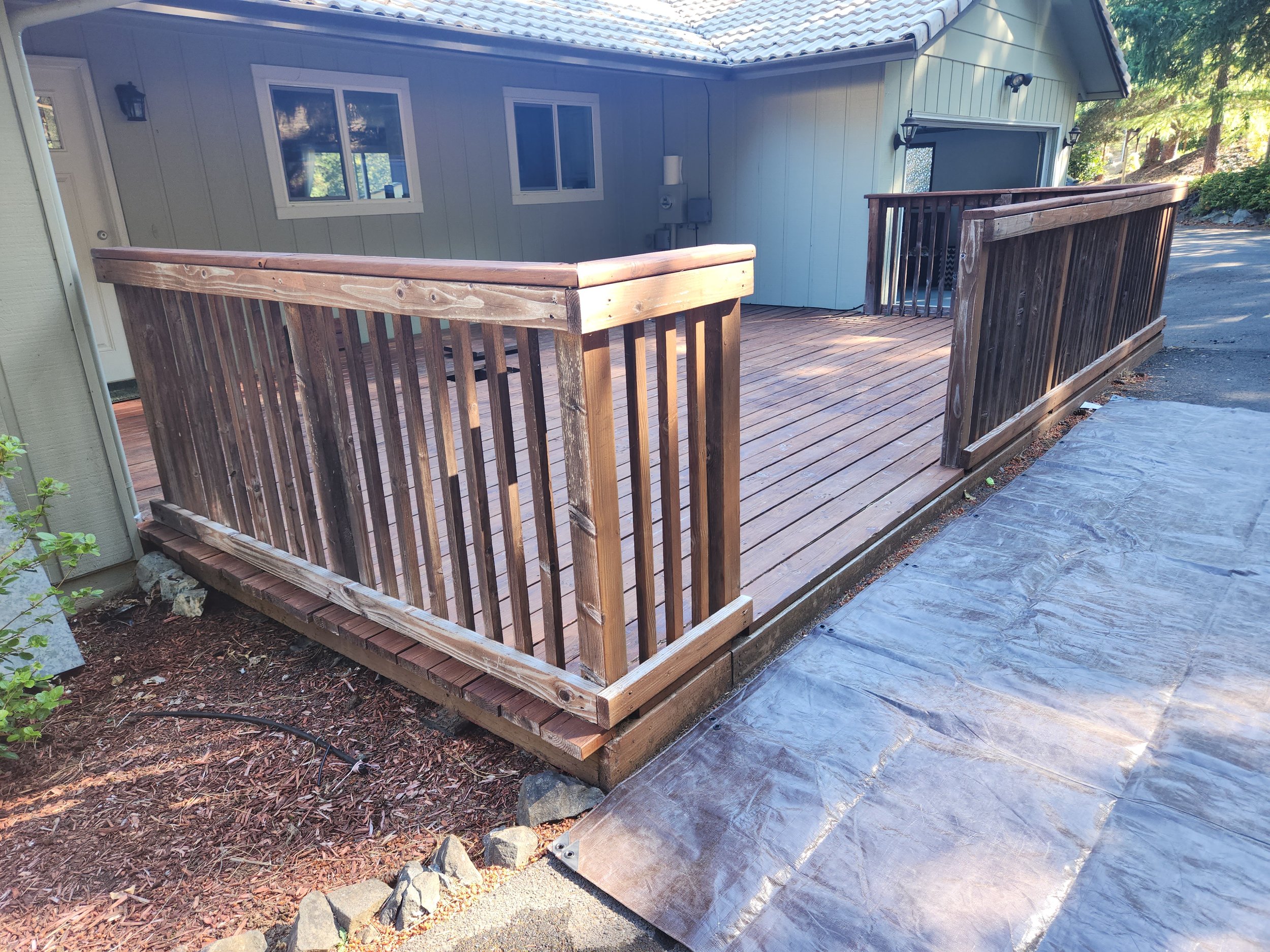 A older weathered deck, with a railing around the edges, surrounded by a yard with trees.