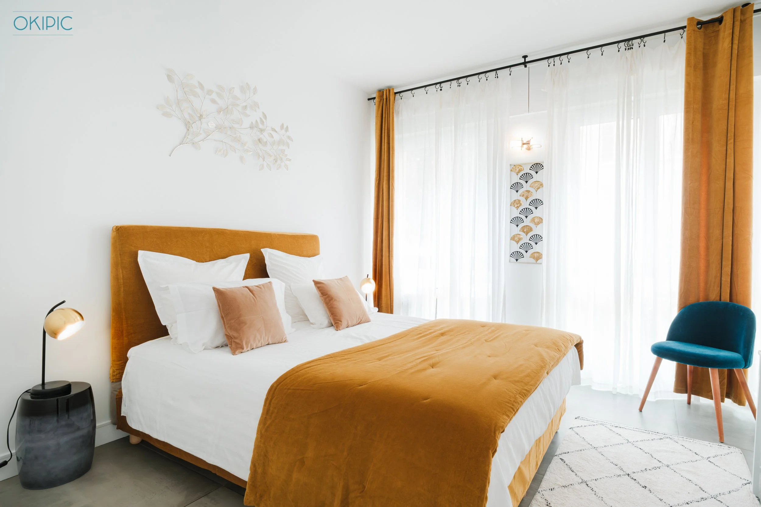 Sunny, stylish bedroom (2) with plush bed, gold accents, and sheer drapes.