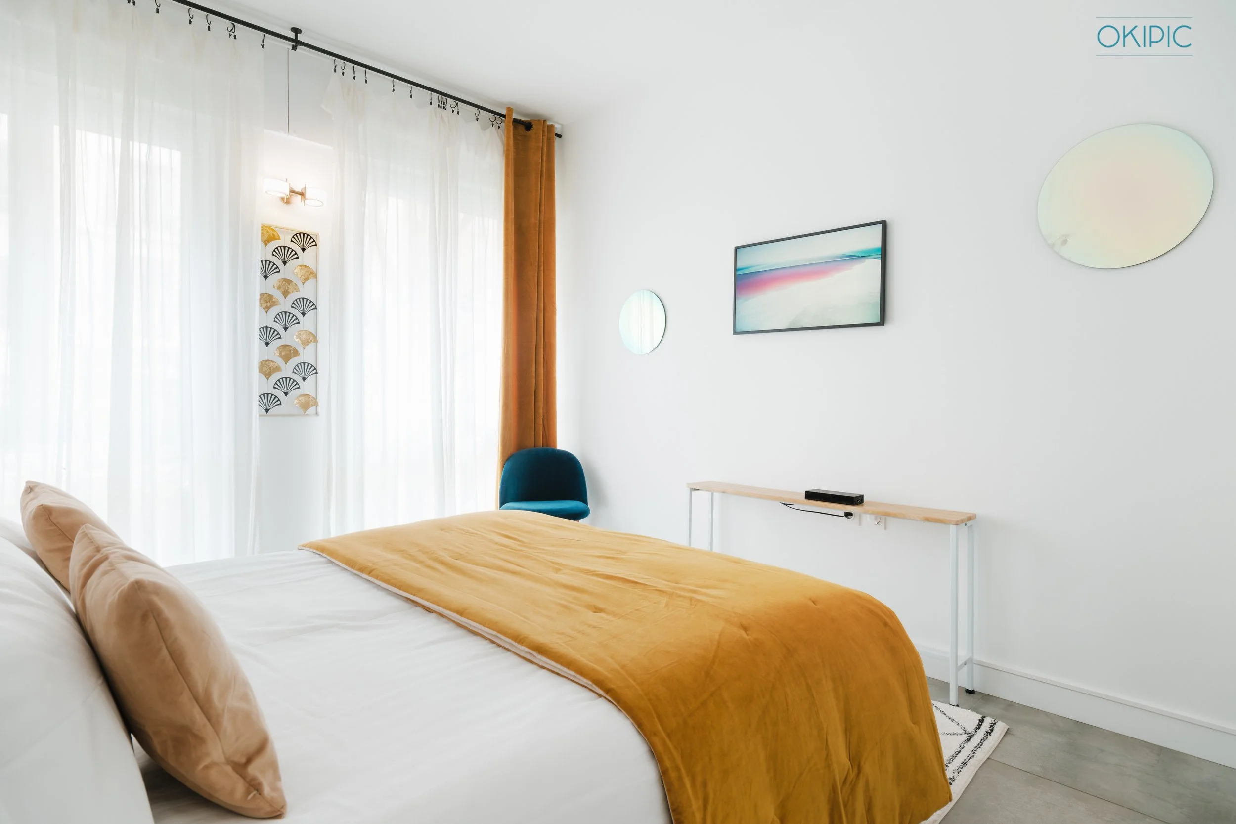 Sunlit minimalist bedroom (2) with plush bed, mustard throw, and TV.