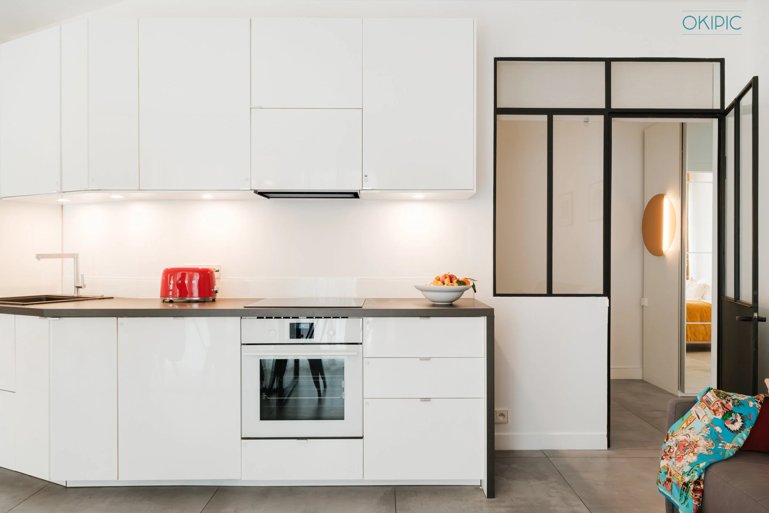 Sleek white kitchen, built-in oven, glass partition to cozy bedroom.