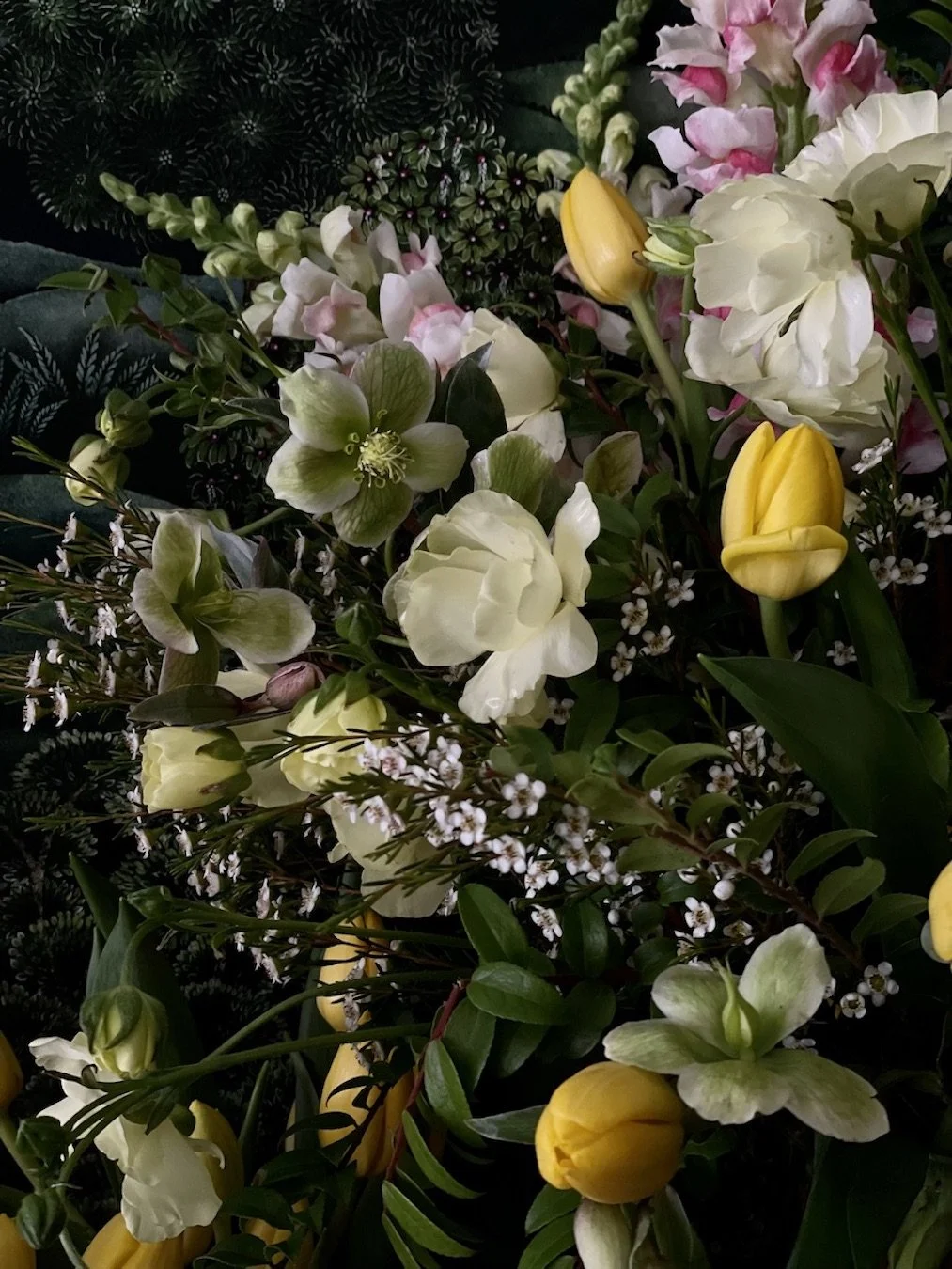 A close-up of a colorful bouquet with white, yellow, and pink flowers, including tulips, in a dark setting.