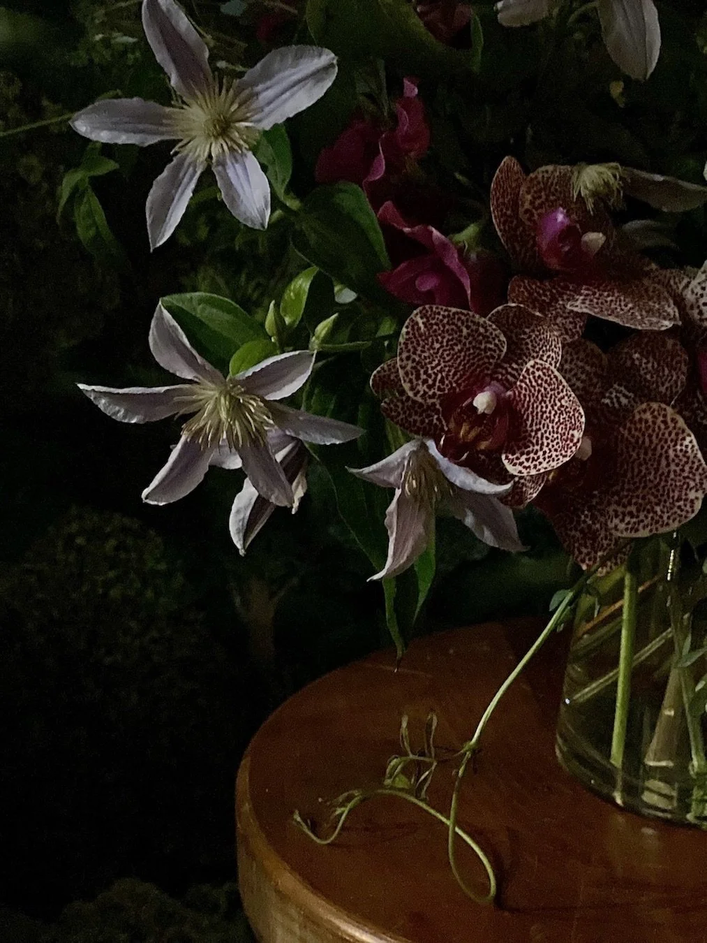Close-up of white and spotted pink orchids in a glass vase on a wooden table.
