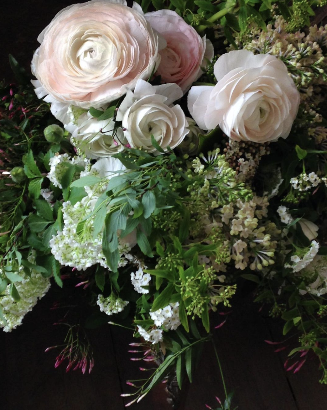 A bouquet of white and pale pink roses with various green leaves and small white flowers amidst dark background.