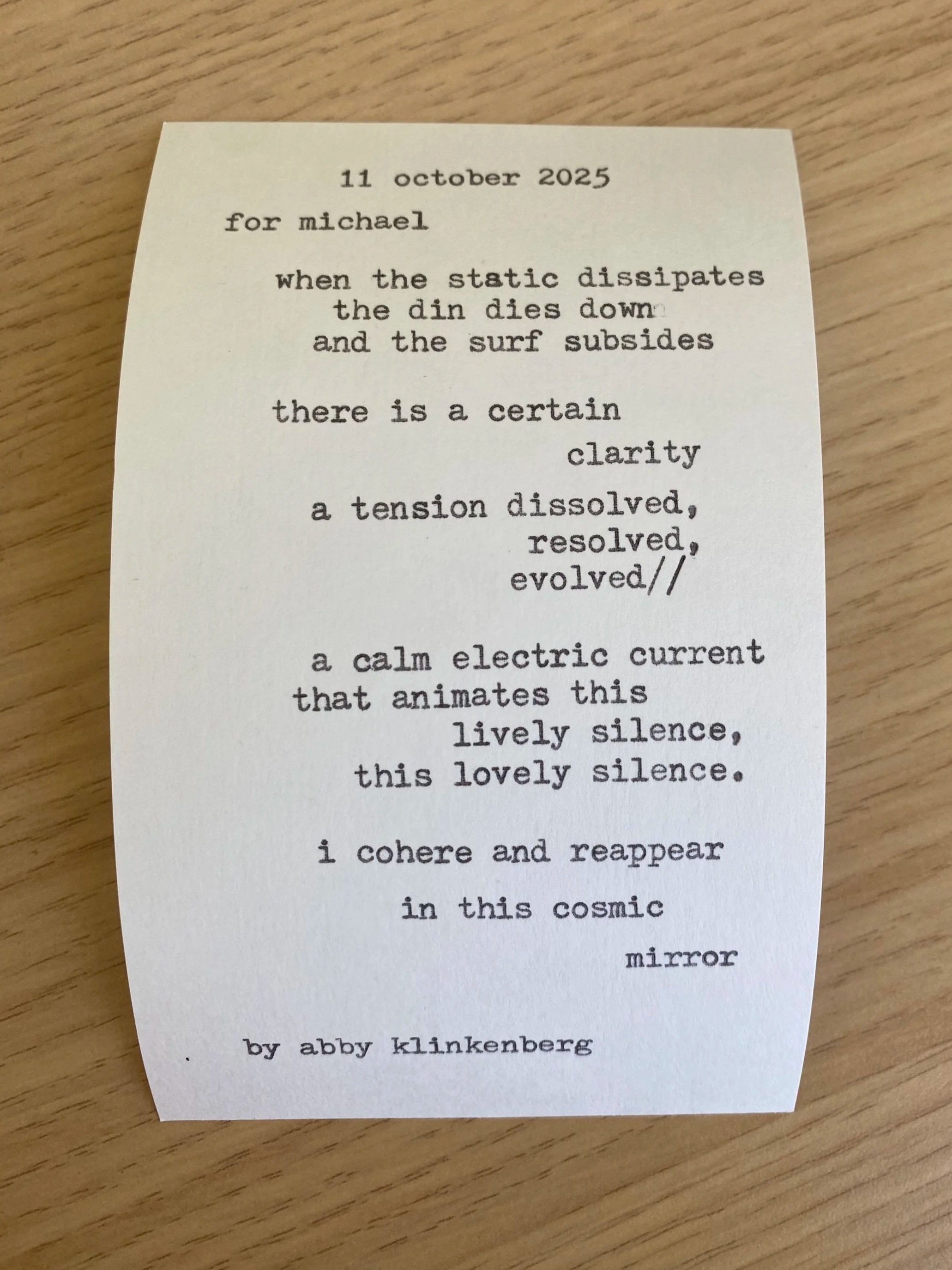 A handwritten note or poem on a small piece of white paper, resting on a wooden surface. The text is typewritten and includes a date, a dedication, and poetic lines.