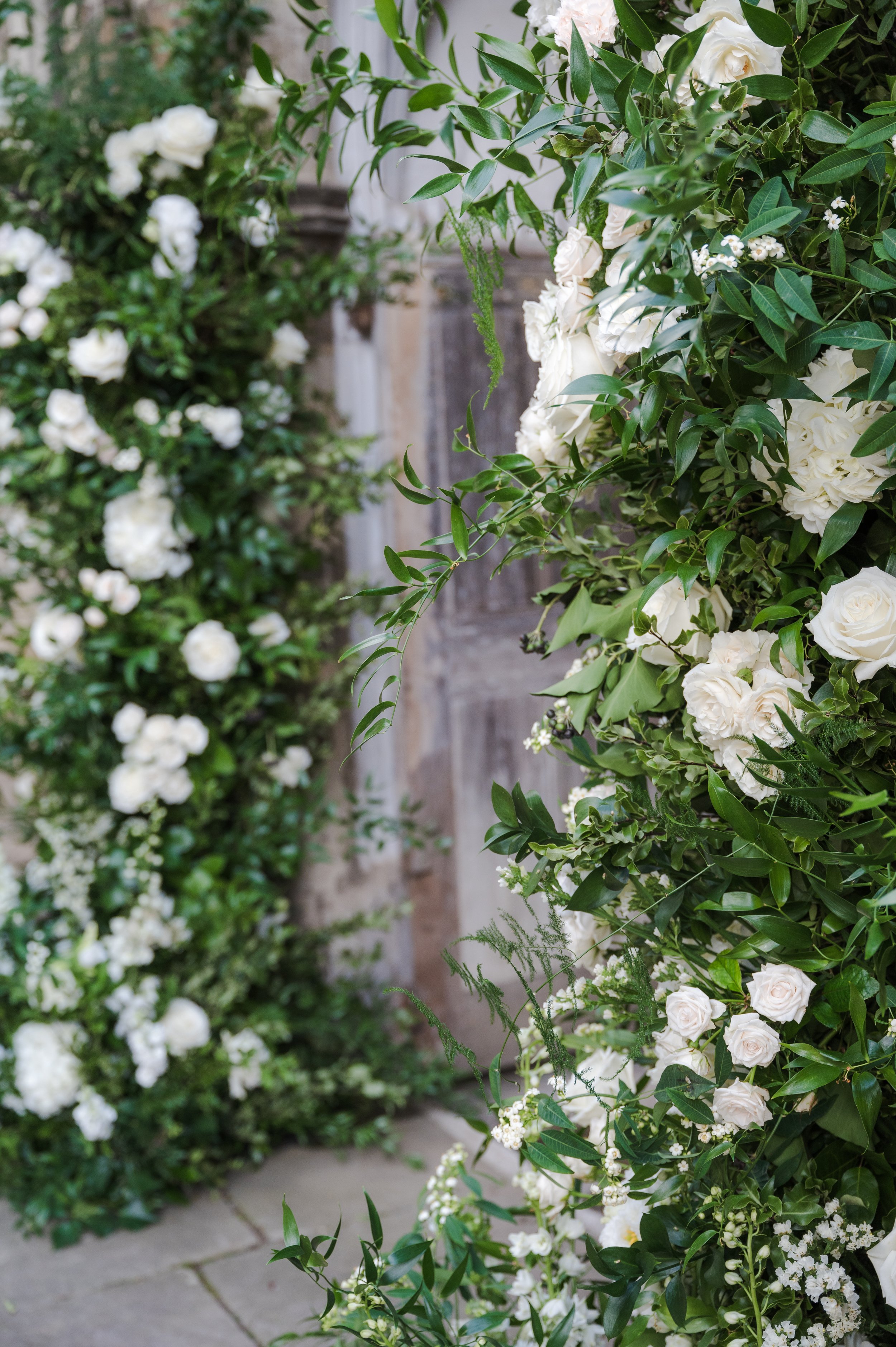 A floral arrangement of white roses, small white flowers, and green foliage placed outdoors.