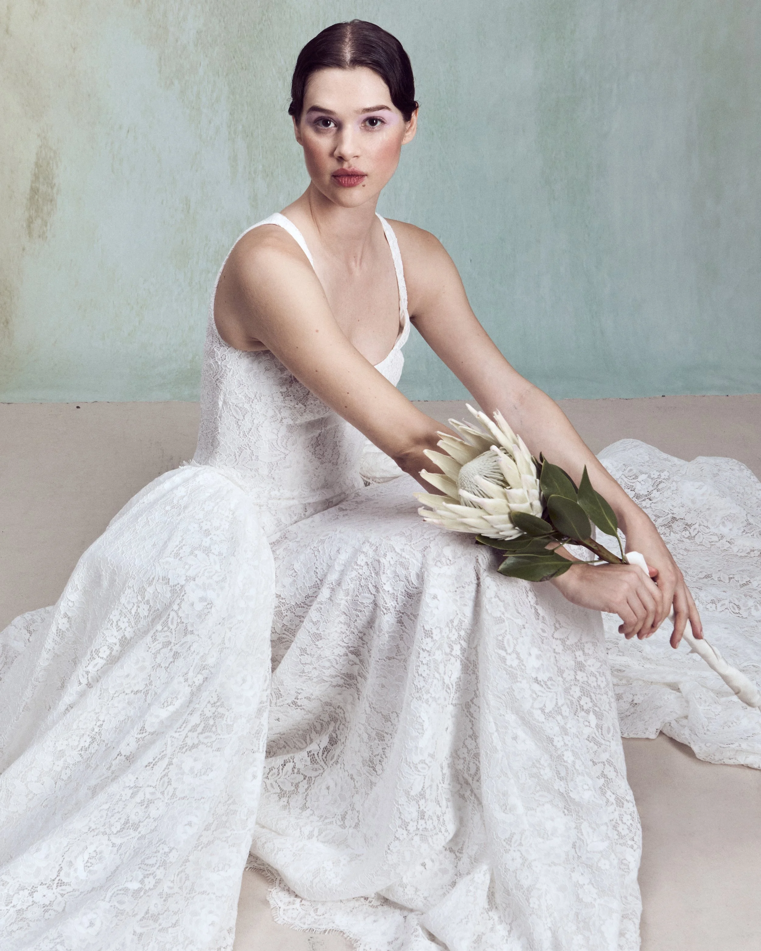 Corded Lace gown with a deep rounded neckline, an independent underwire bustier, and continuous lace-up detailing extending the length of the back, paired with a removable architectural overskirt.
