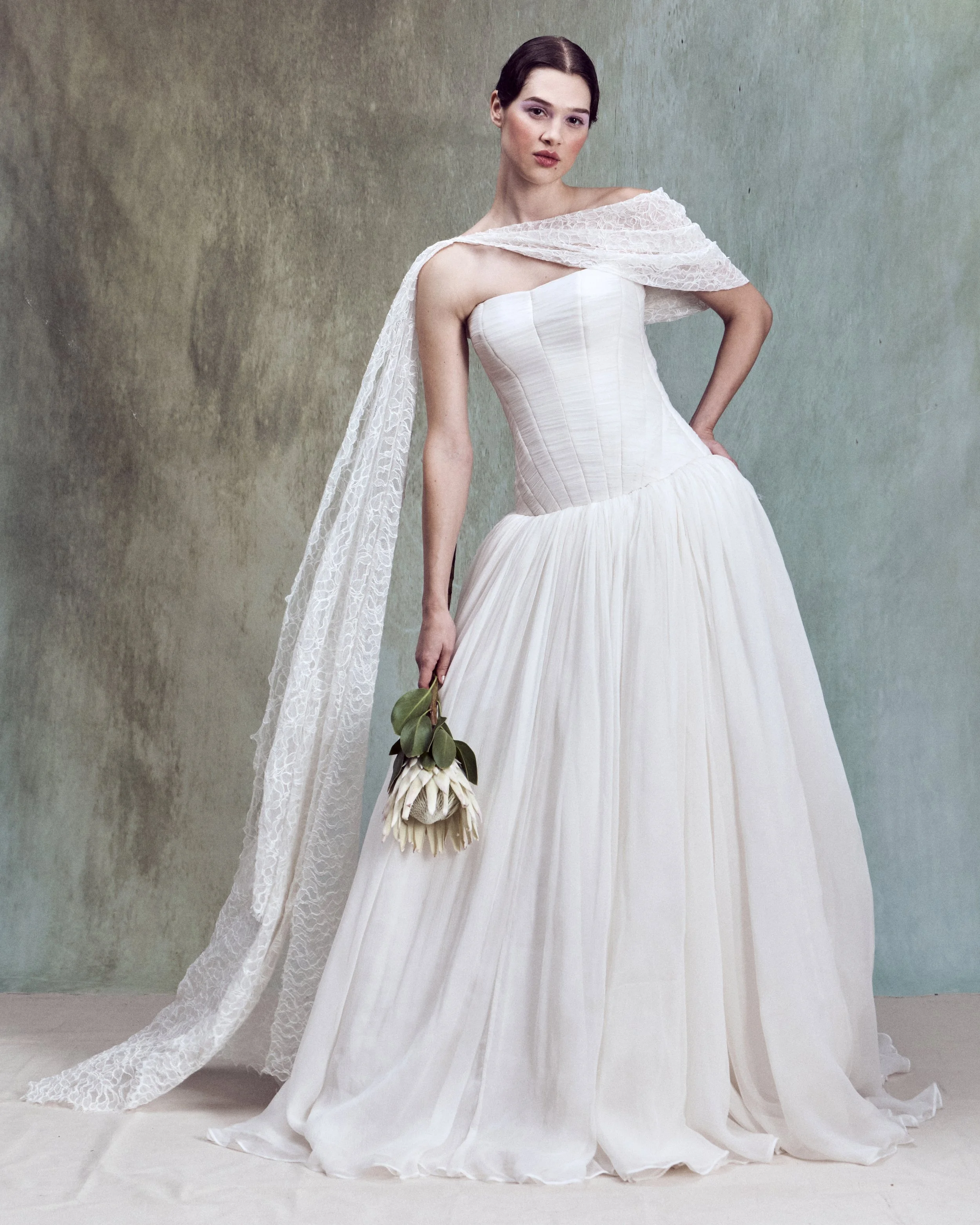 Crinkled Silk Chiffon gown with diagonal hand-draped motifs and drop-waist bustier with circle skirt, paired with an off-the-shoulder asymmetrical corded lace cape with a flowing draped panel.
