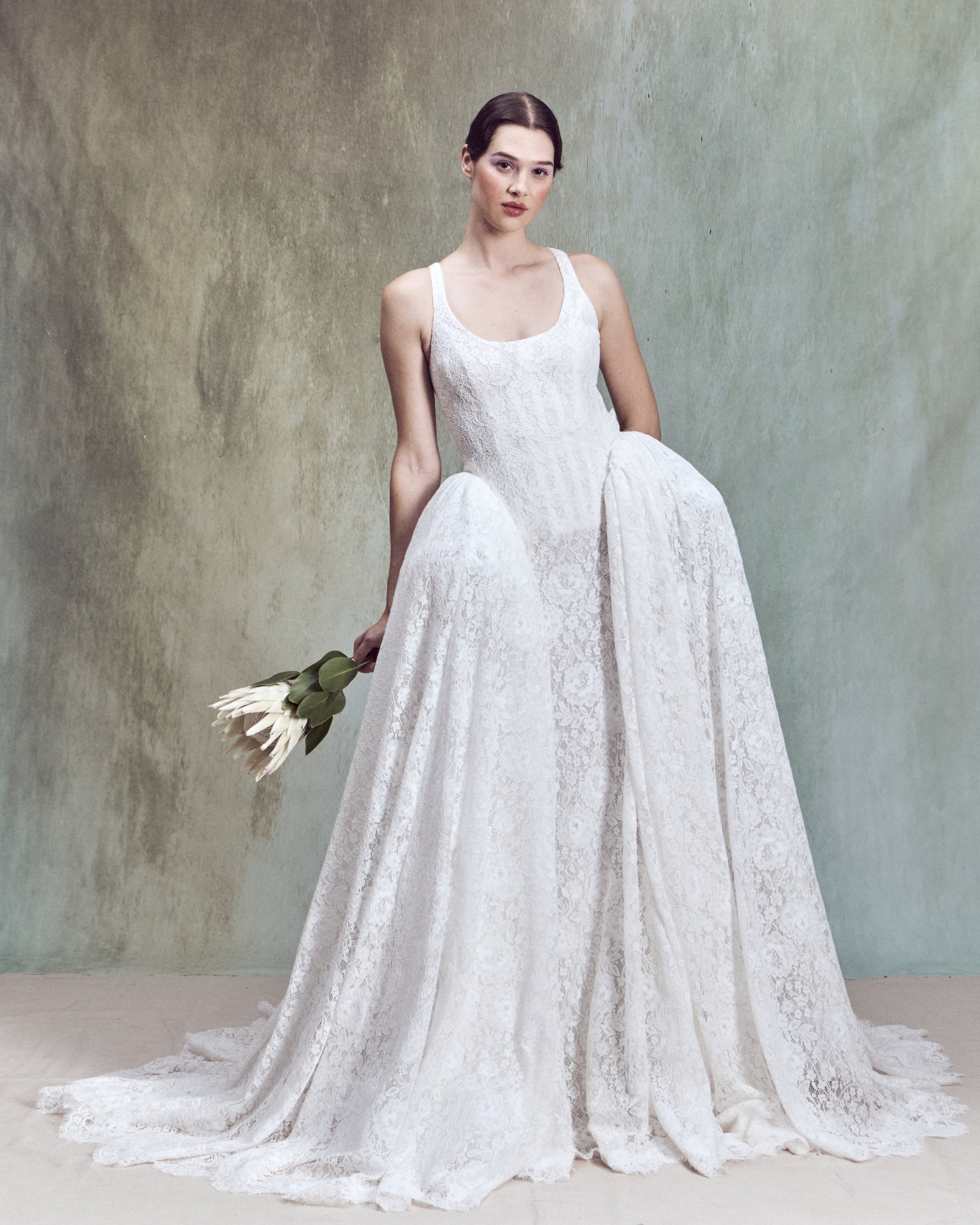 Corded Lace gown with a deep rounded neckline, an independent underwire bustier, and continuous lace-up detailing extending the length of the back, paired with a removable architectural overskirt.