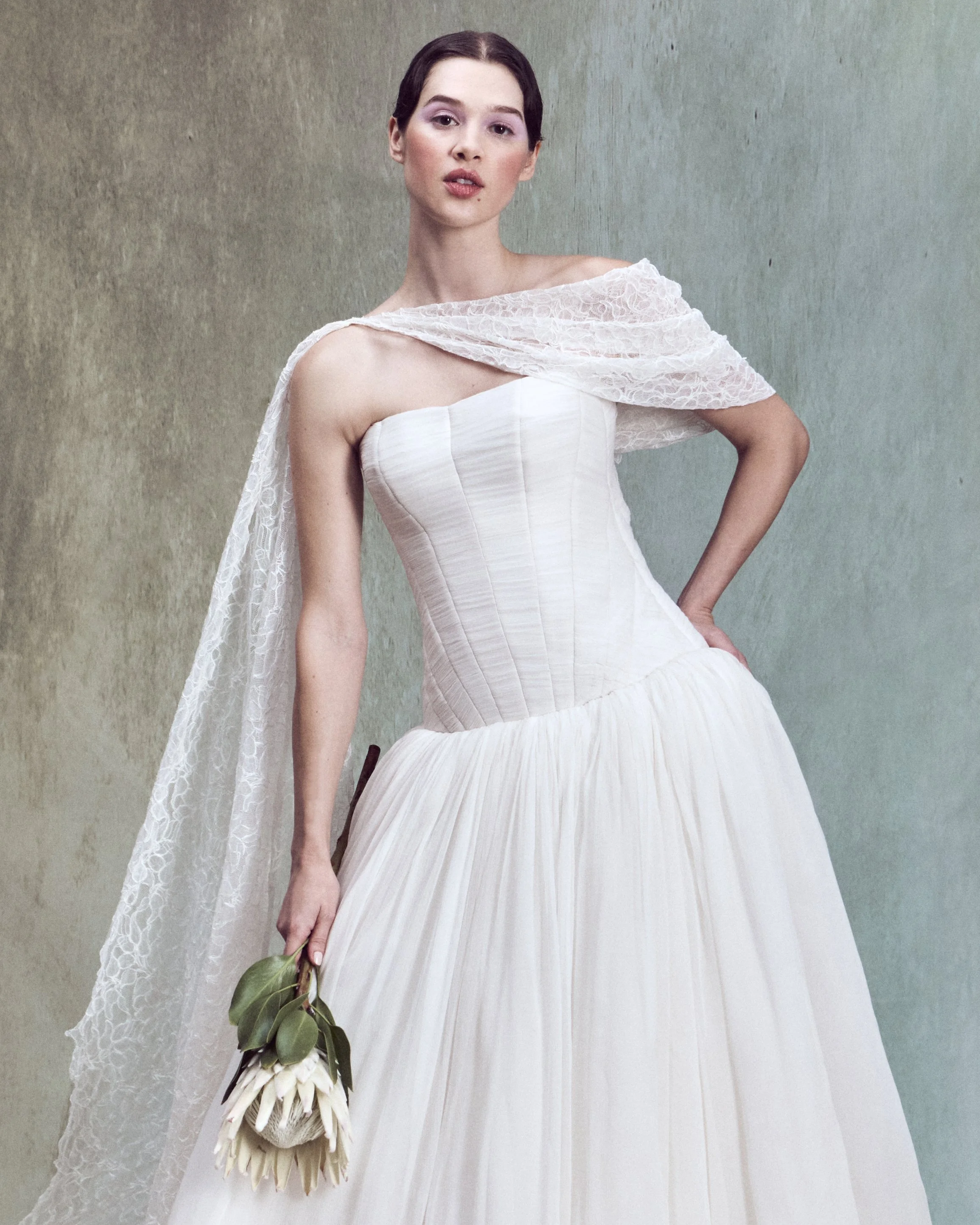 Crinkled Silk Chiffon gown with diagonal hand-draped motifs and drop-waist bustier with circle skirt, paired with an off-the-shoulder asymmetrical corded lace cape with a flowing draped panel.