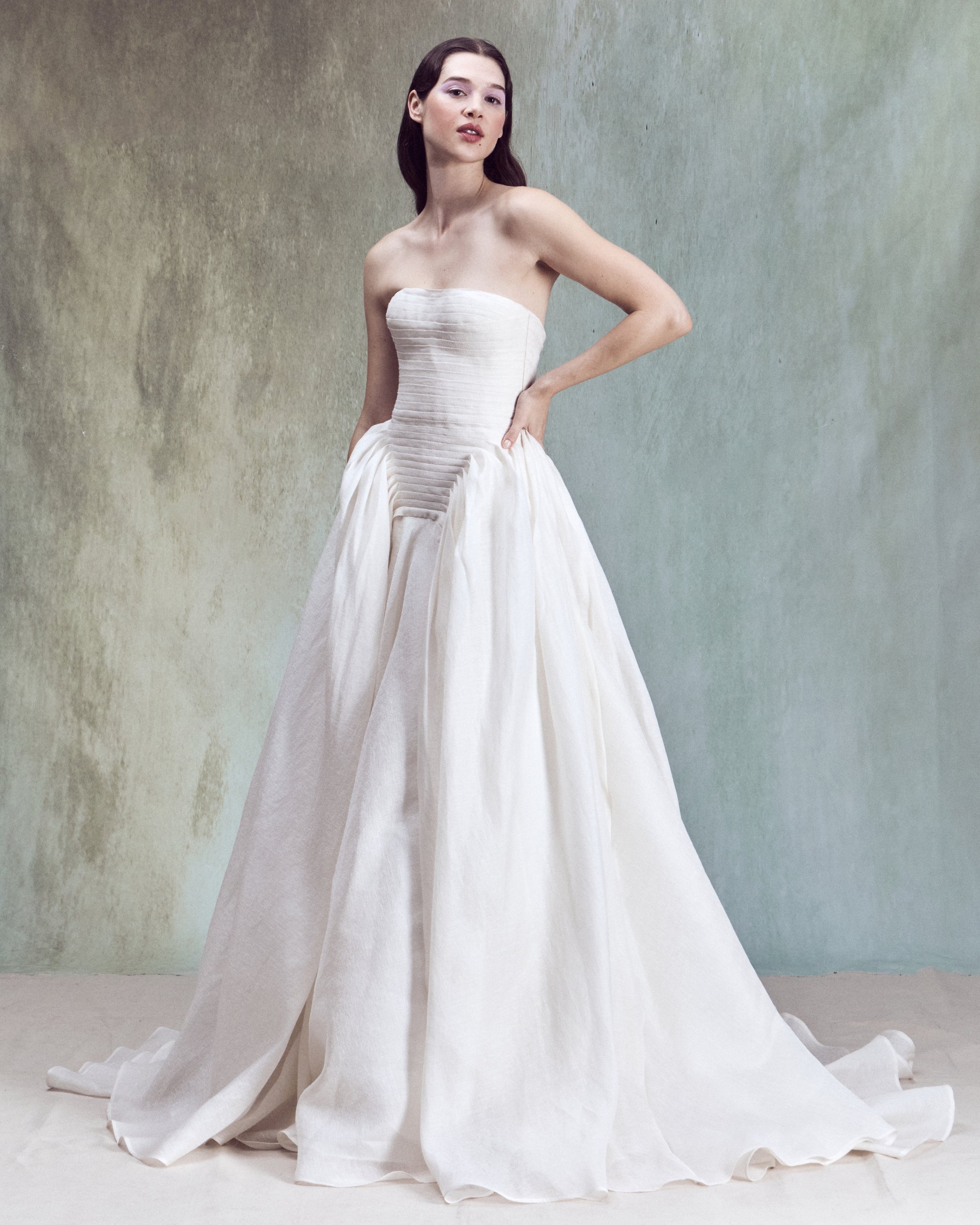 Strapless Silk Linen ball gown with a drop-waist bustier, horizontal hand-pleated draping, and full skirt with exaggerated volume at the sides.