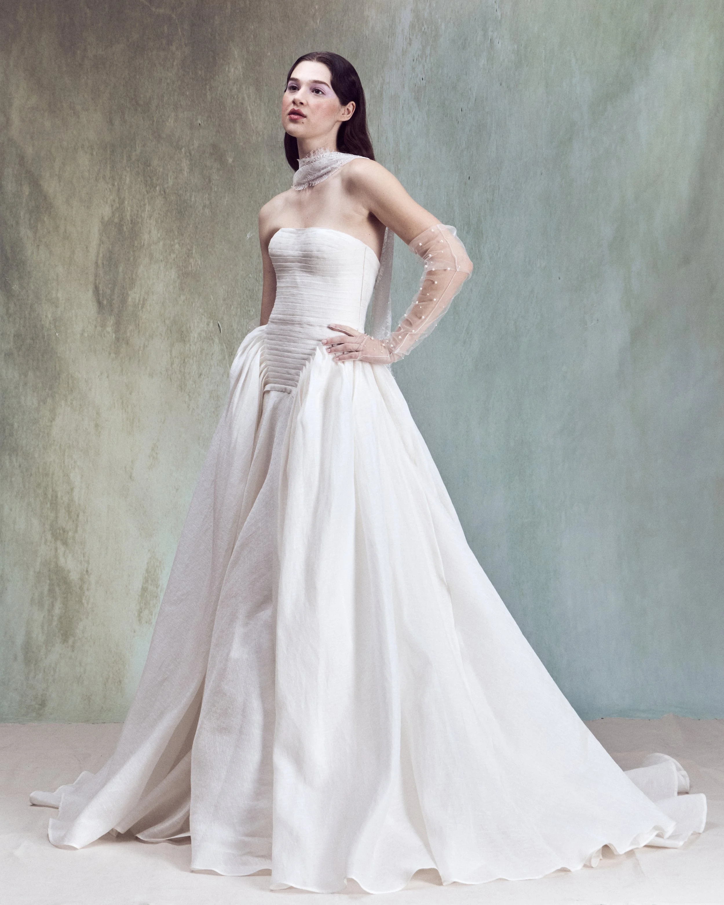 Strapless Silk Linen ball gown with a drop-waist bustier, horizontal hand-pleated draping, and full skirt with exaggerated volume at the sides.
