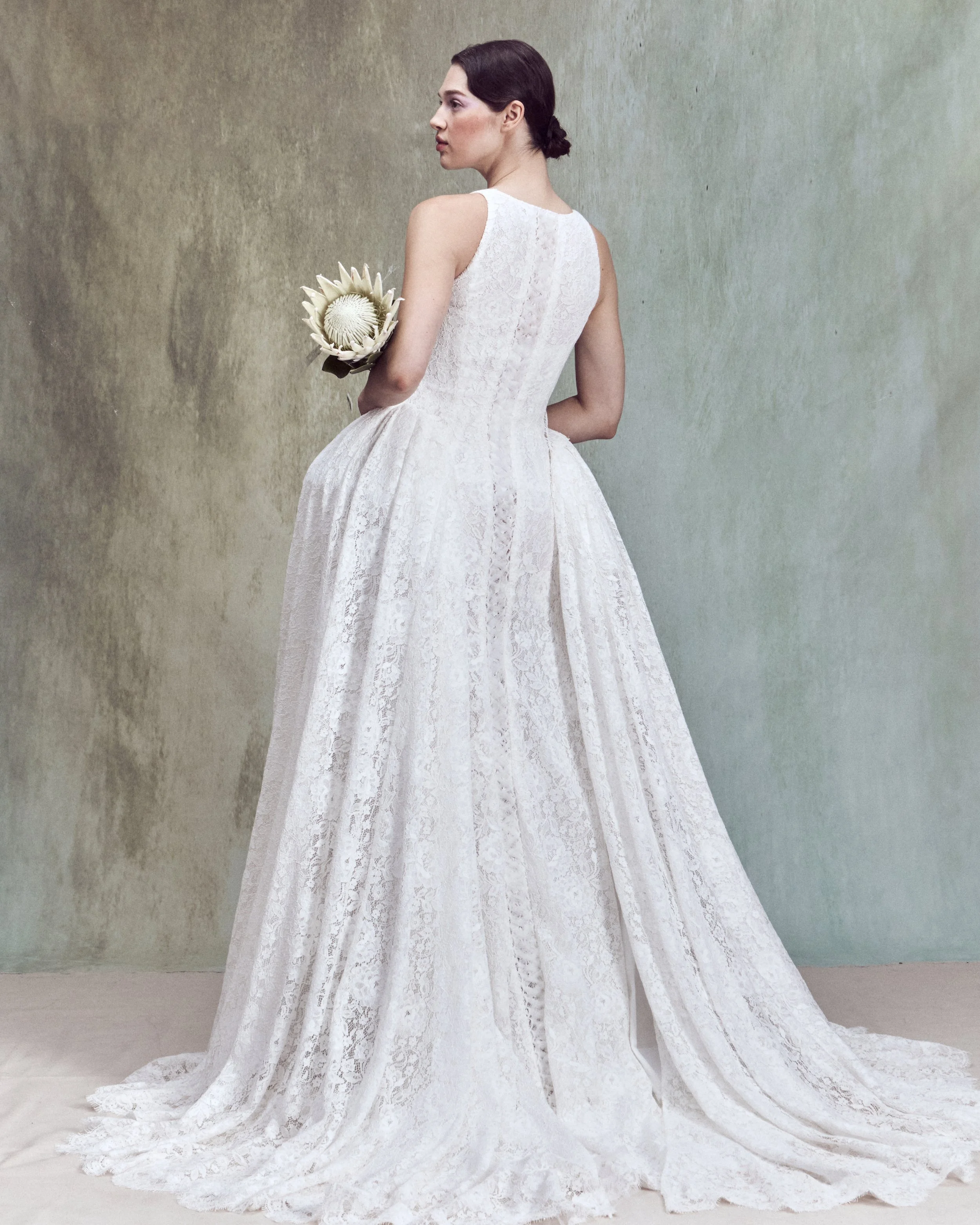 Corded Lace gown with a deep rounded neckline, an independent underwire bustier, and continuous lace-up detailing extending the length of the back, paired with a removable architectural overskirt.