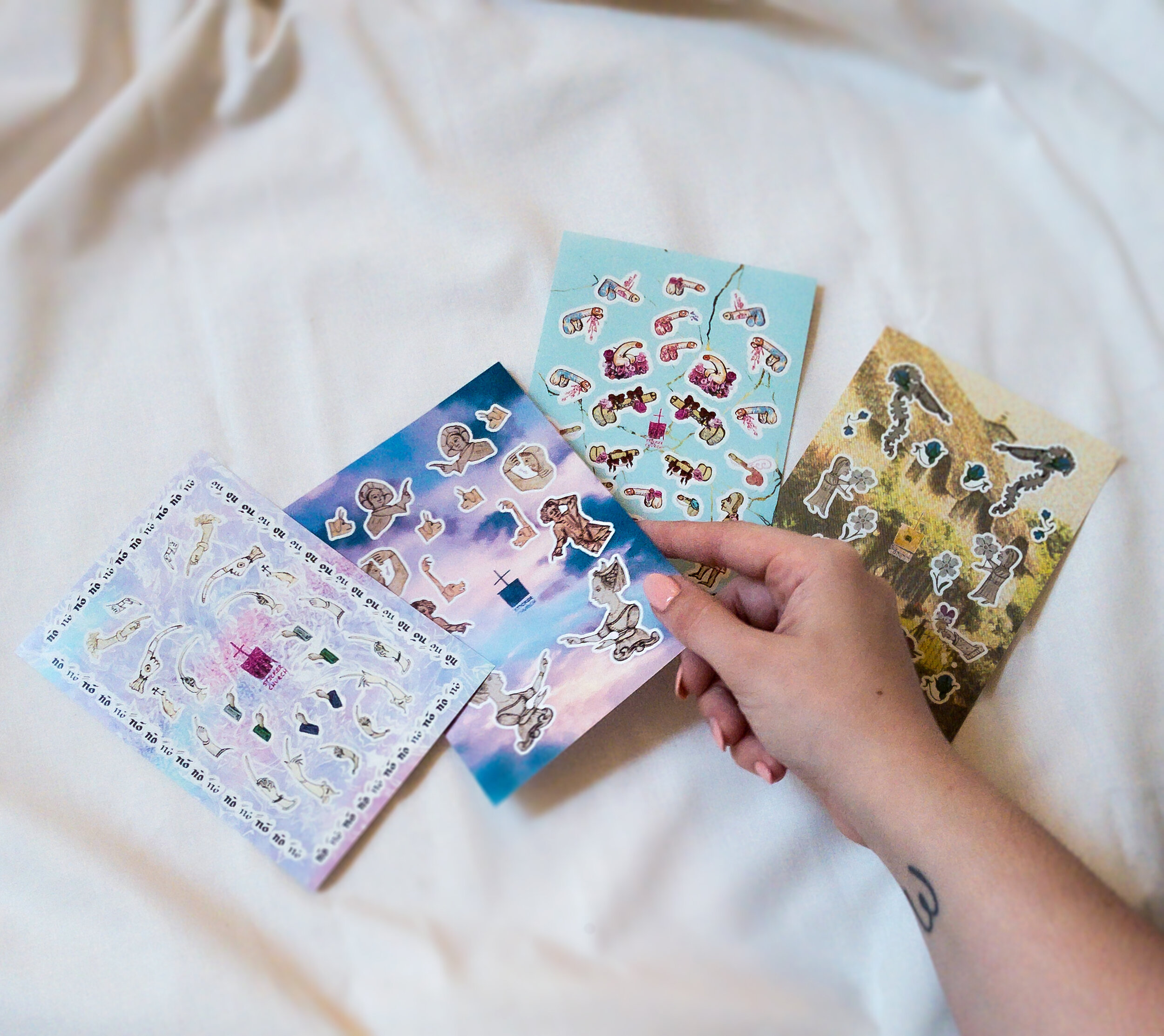 All 4 sticker sheets in the Pointing Fingers collection are fanned out on a neutral background. A hand with a pale coral manicure reaches to select one of the sheet.