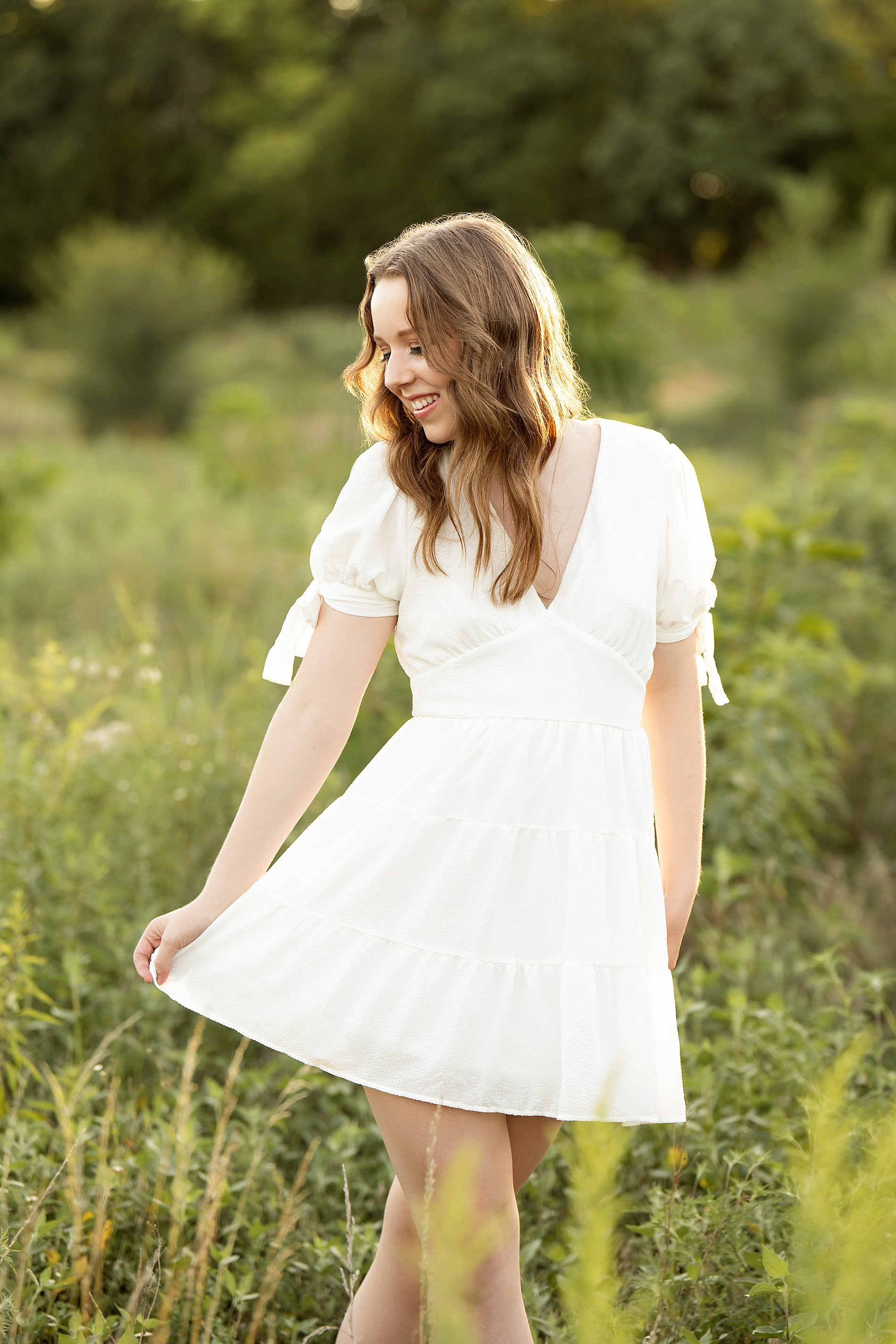  senior twirls in white dress in field of tall grass during summer senior session 