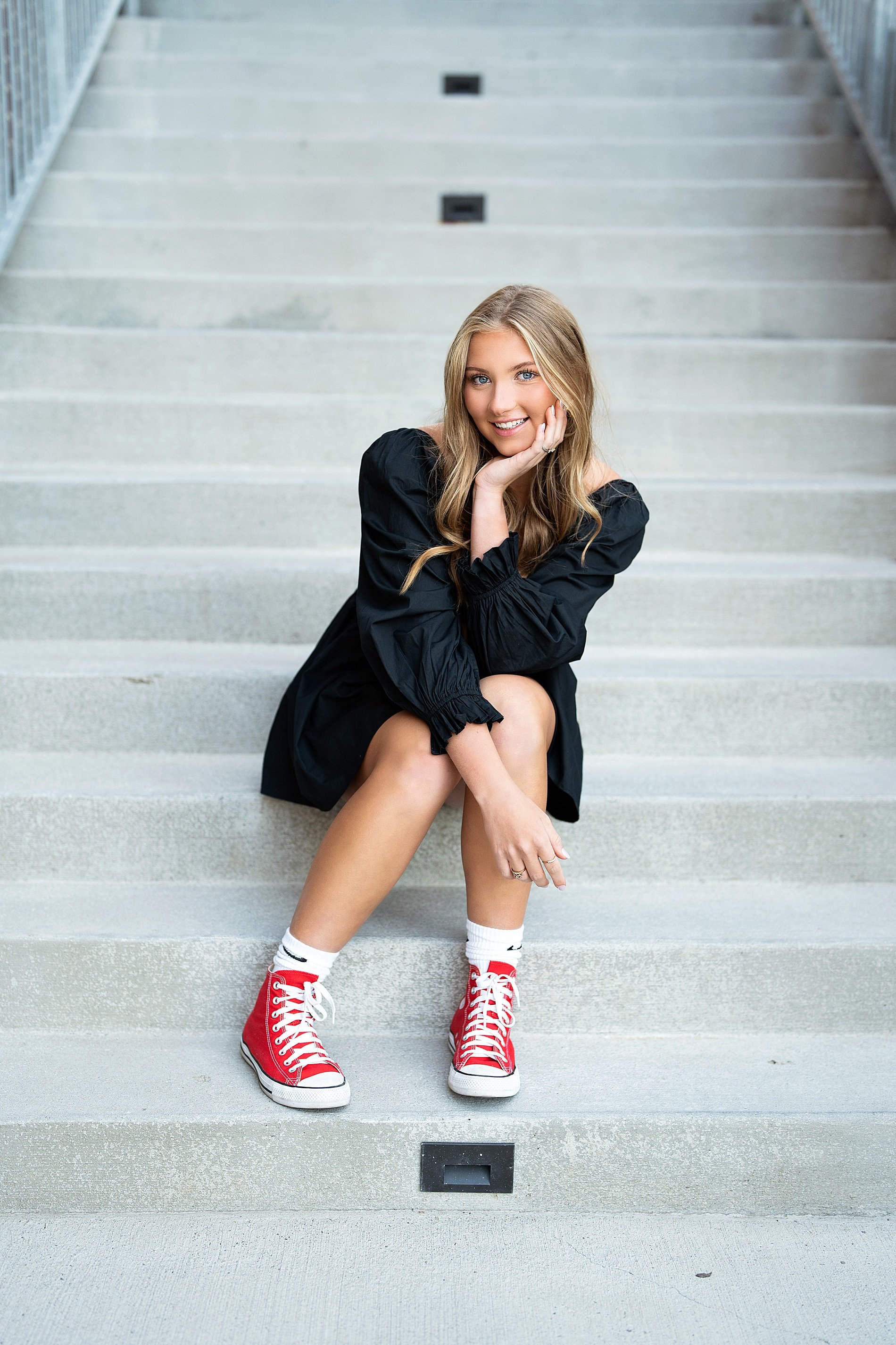  senior girl in black dress and red converse sits on steps  